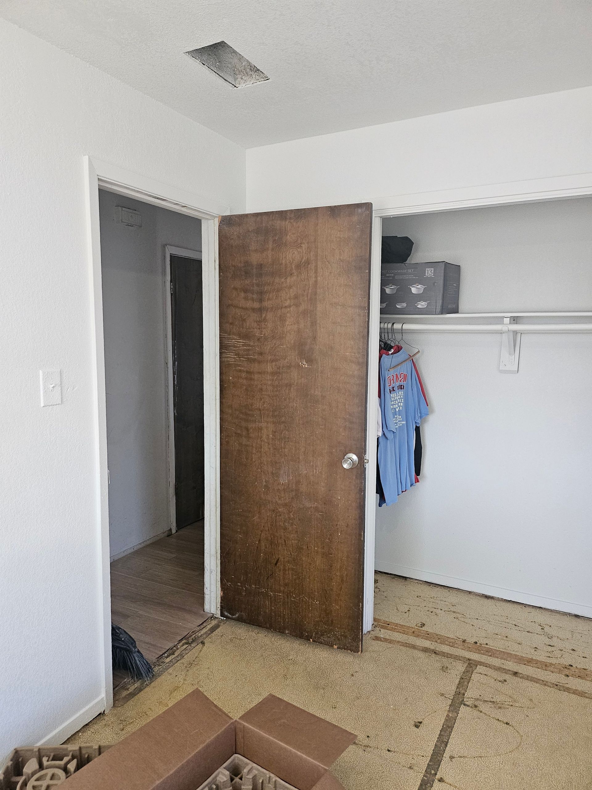 Interior view of a room with open closet, doorway, and box on floor. The door is brown, and walls are white.