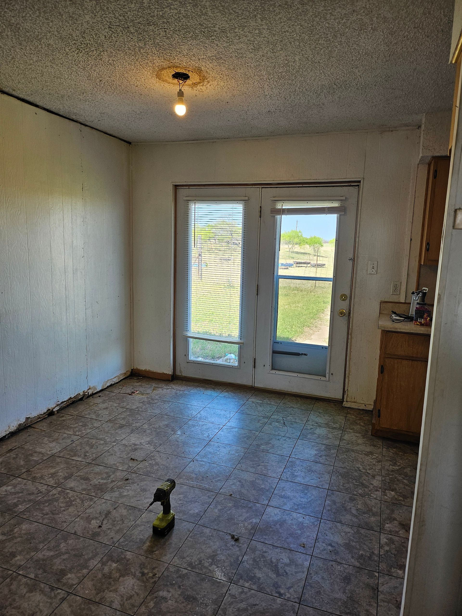 Empty room with French doors, a screw gun, and a light fixture; view of outdoor pasture.