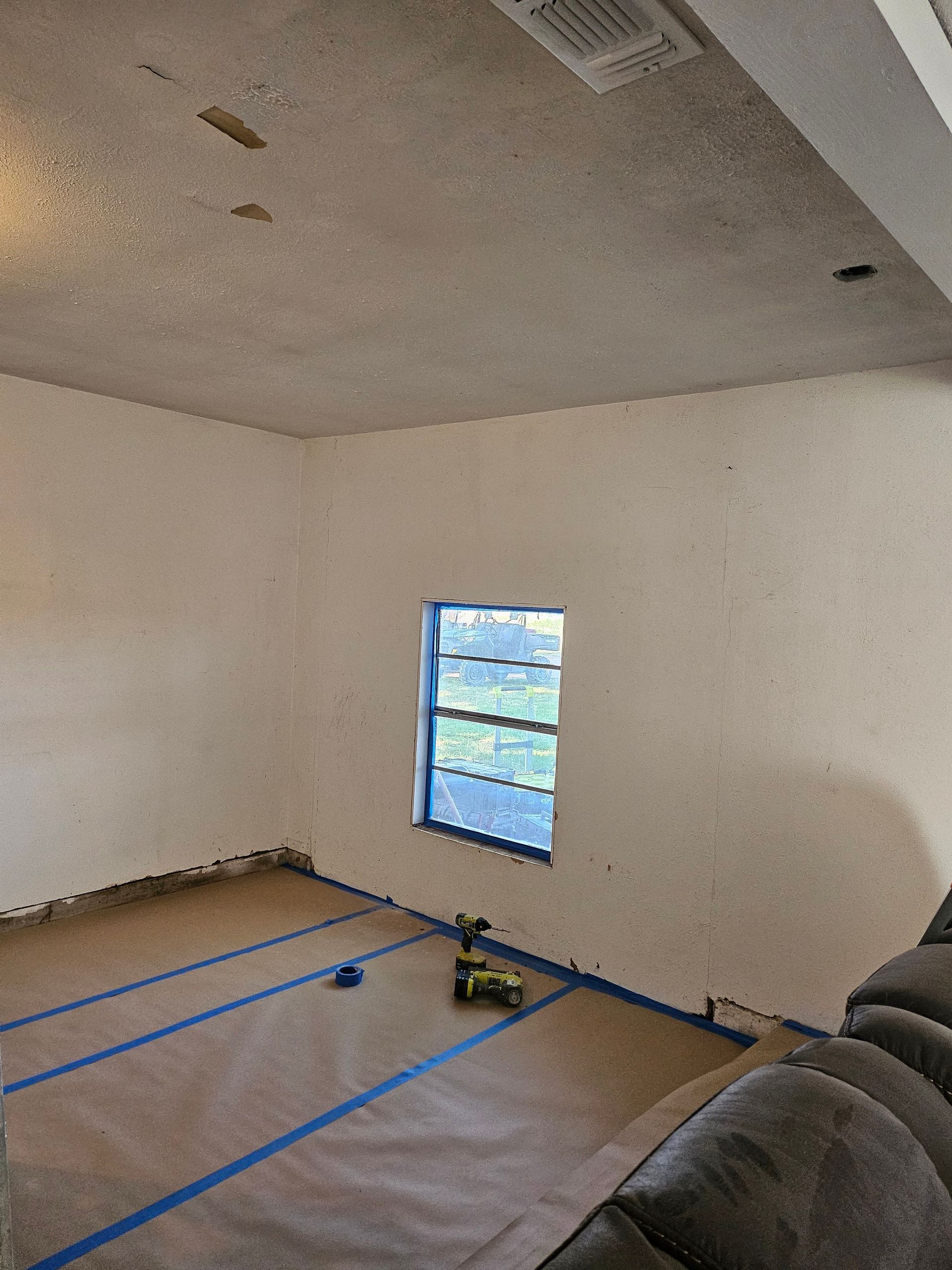 Room with beige walls, small window, and tape along the floor; prepared for painting.
