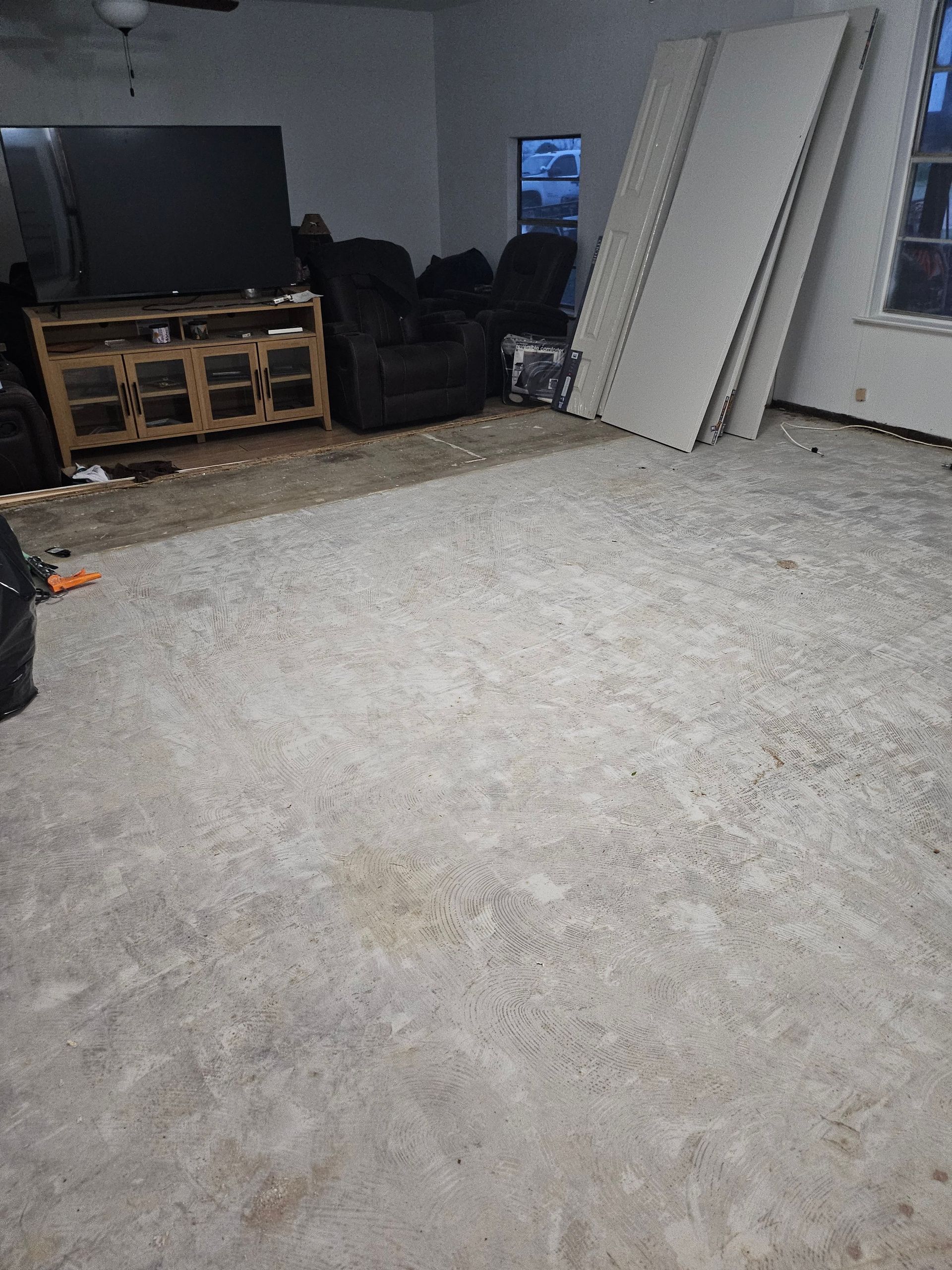 A room with a concrete floor, a TV, furniture, and sheetrock leaning against a wall.