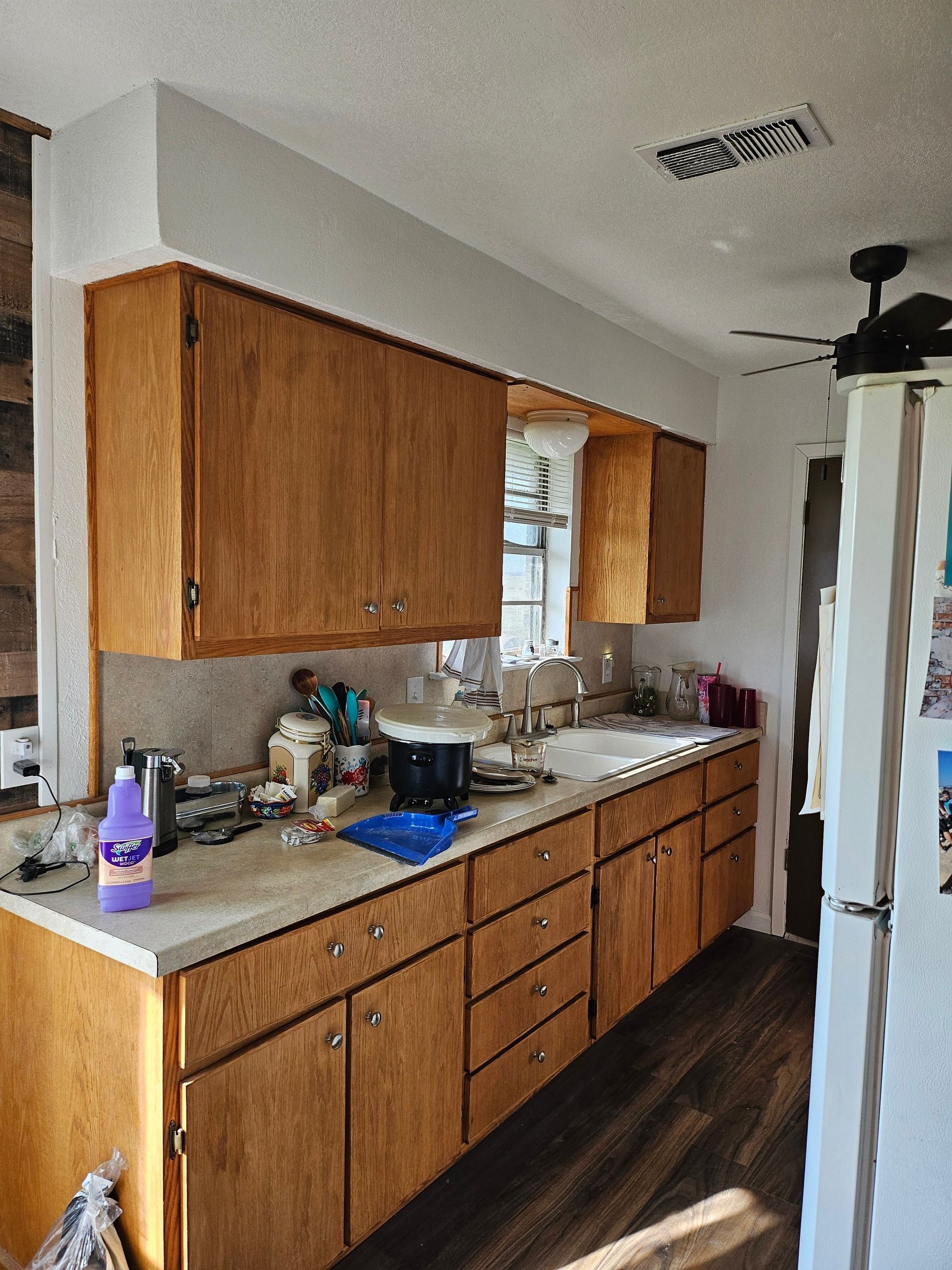 Kitchen with light-colored cabinets, white countertops, and wood-look flooring. A refrigerator is on the right.