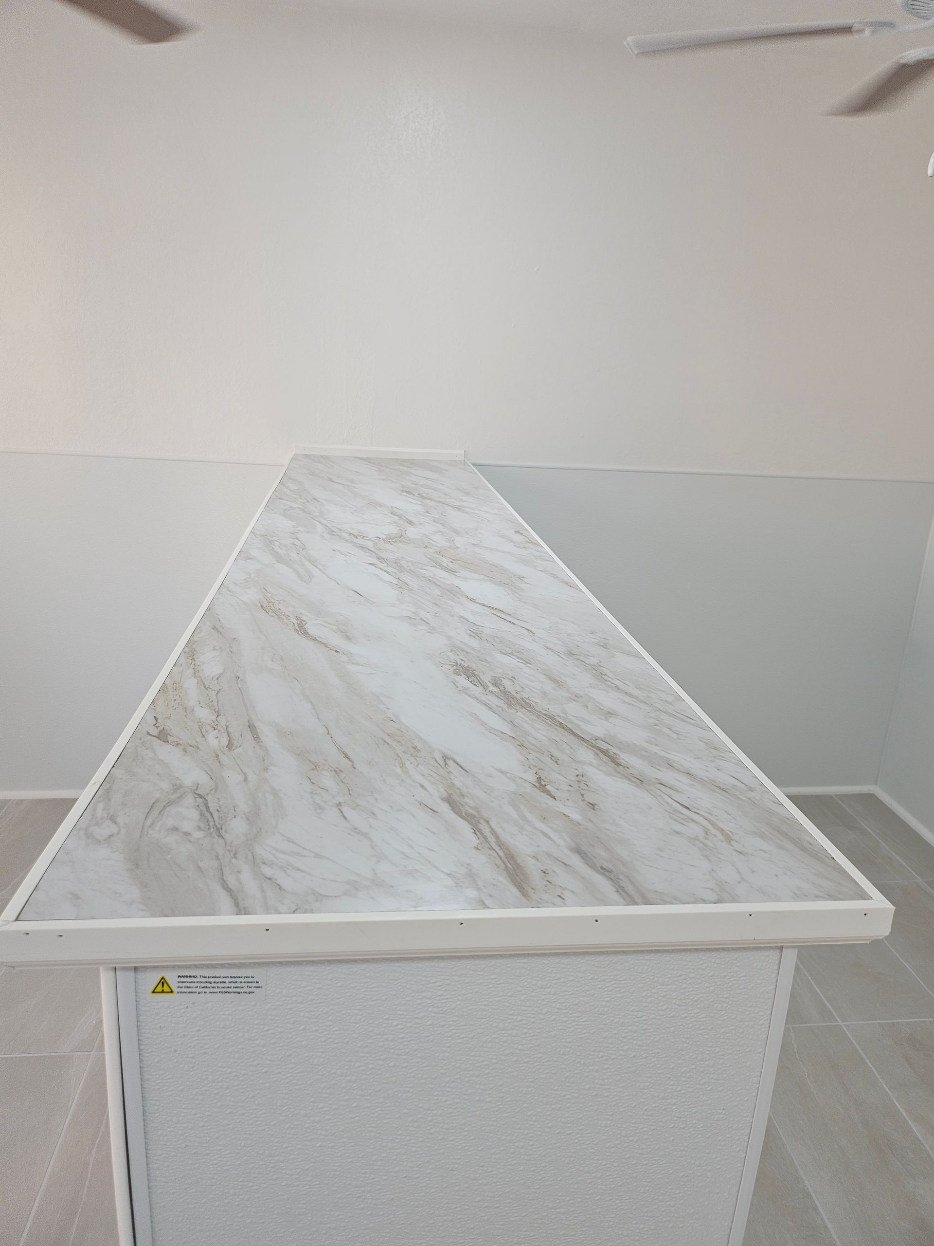 A kitchen island with a light-colored, patterned countertop. The island is rectangular with white paneling.