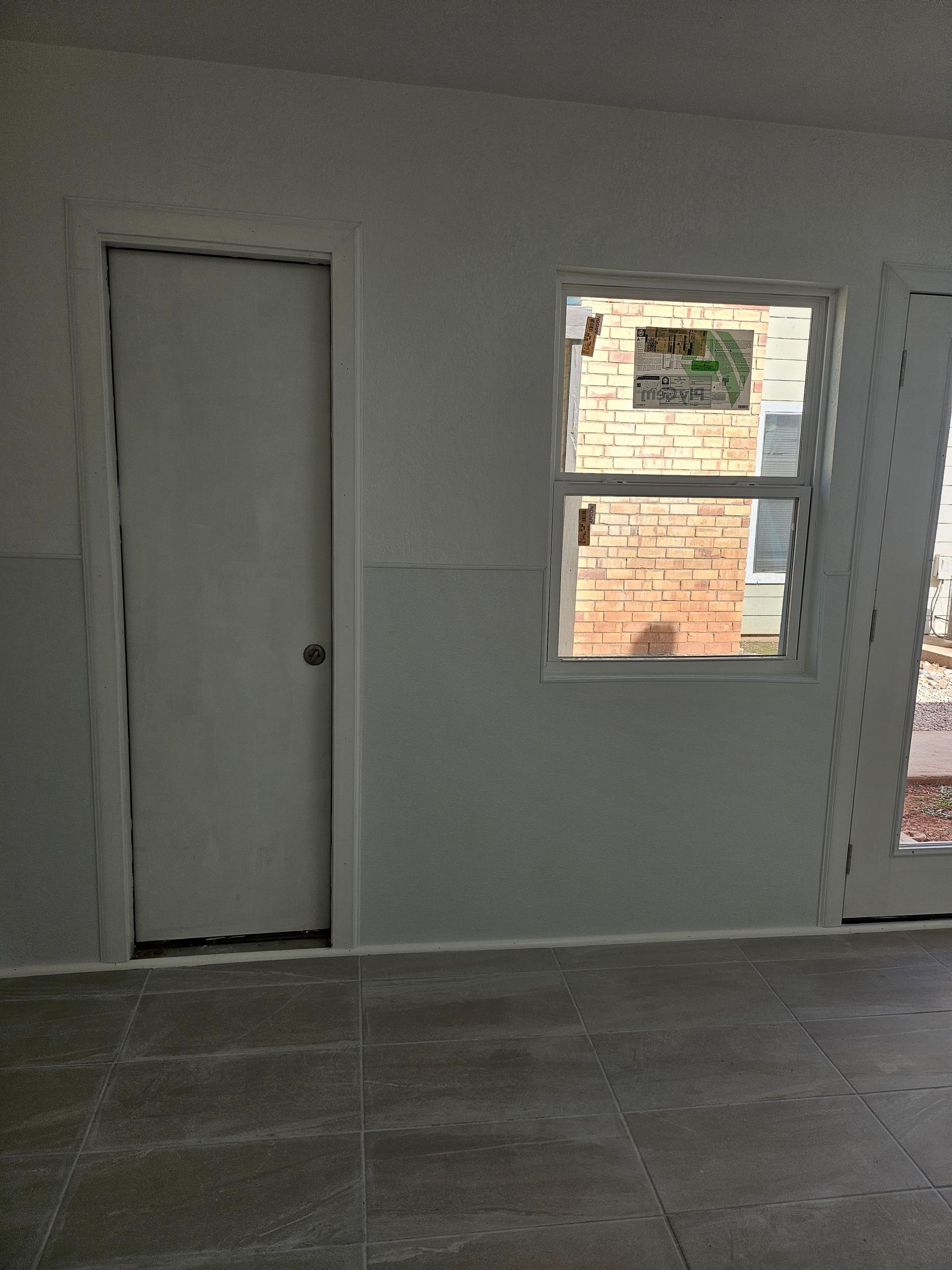 White-walled room with a closed door, window, and sliding glass door; brick building seen through the window.