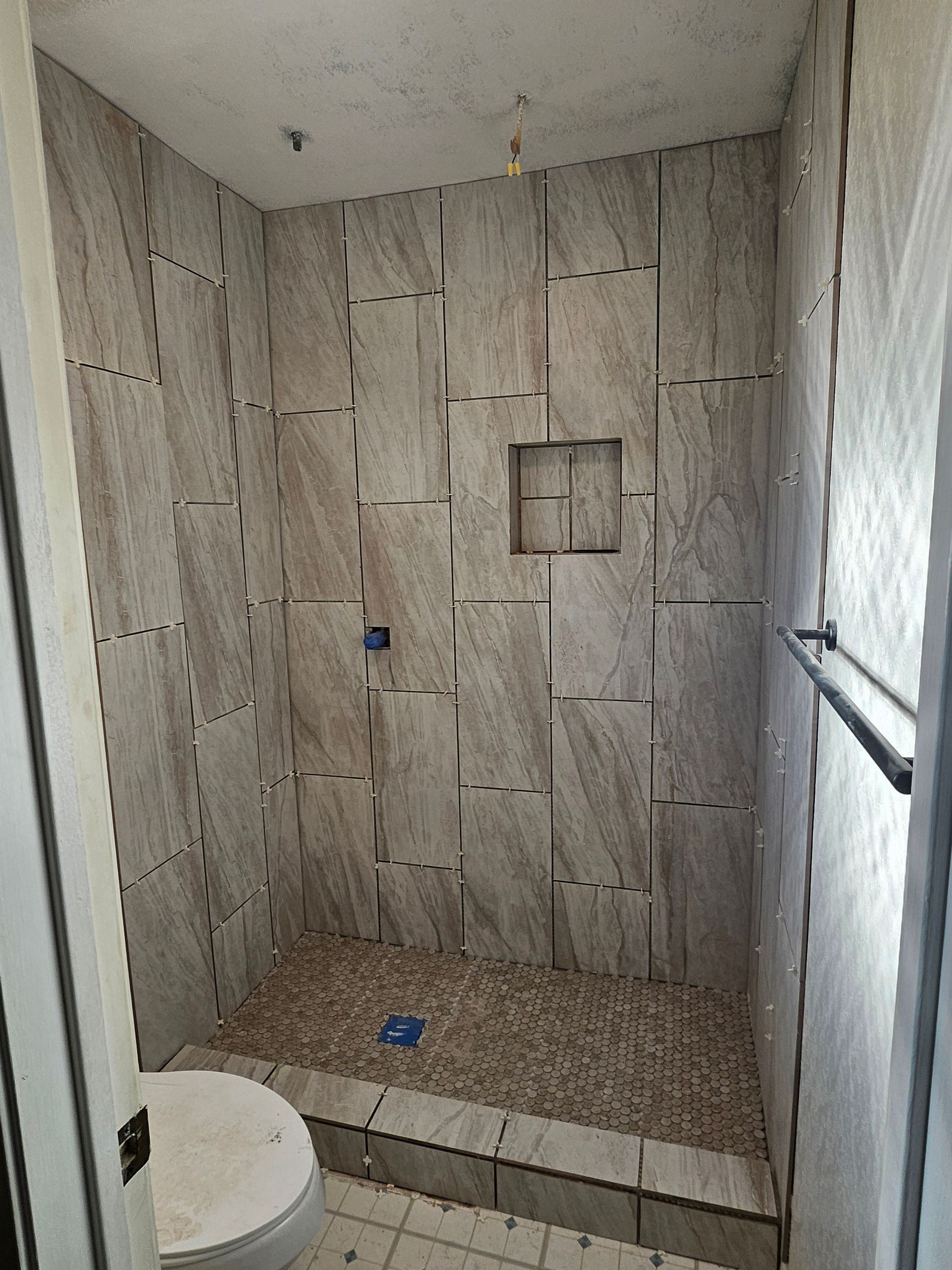 Tiled shower with pebble floor, built-in shelf, and towel rack.