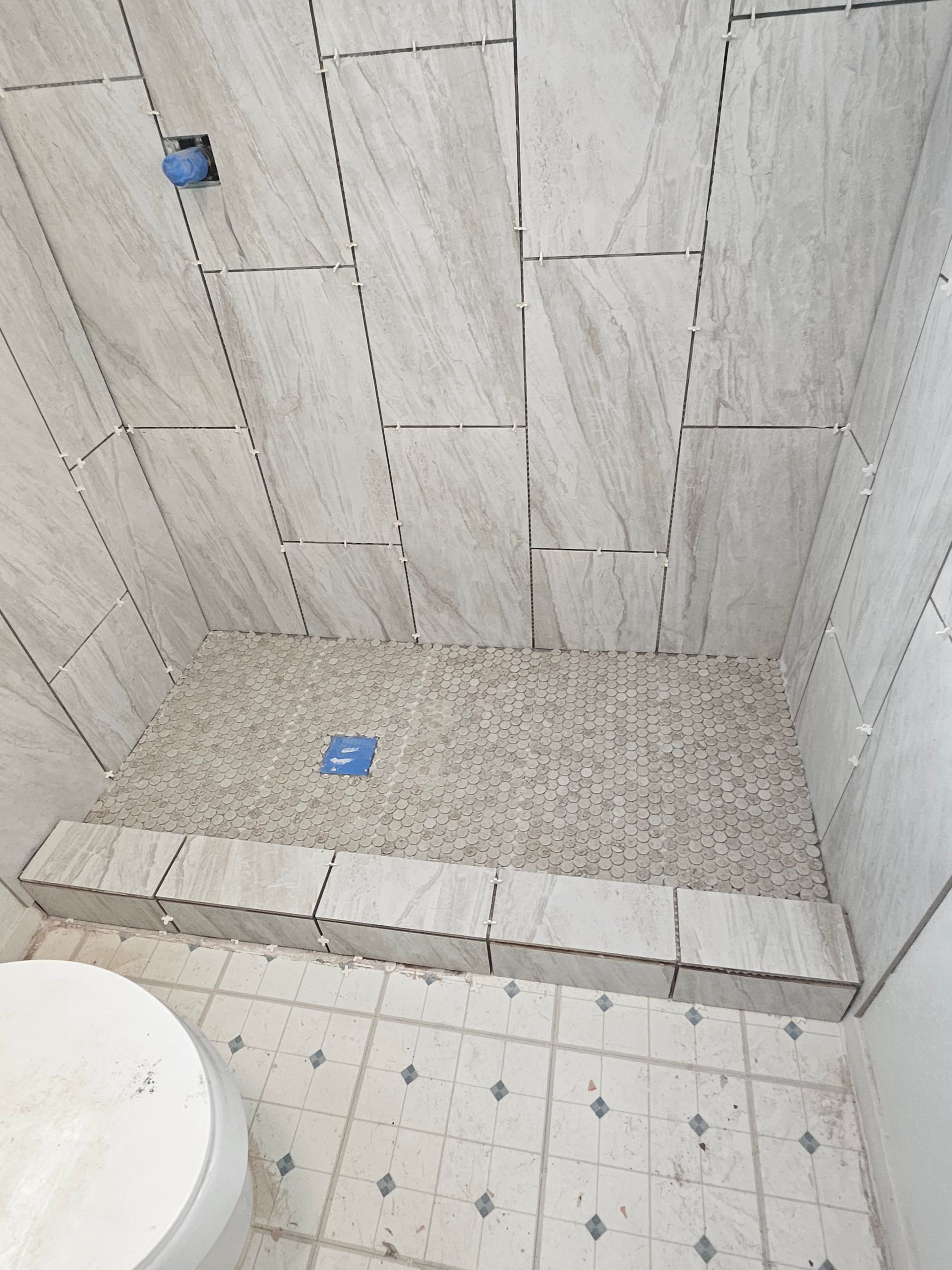 Shower with tile walls and a pebble floor, adjacent to a toilet and tiled floor.