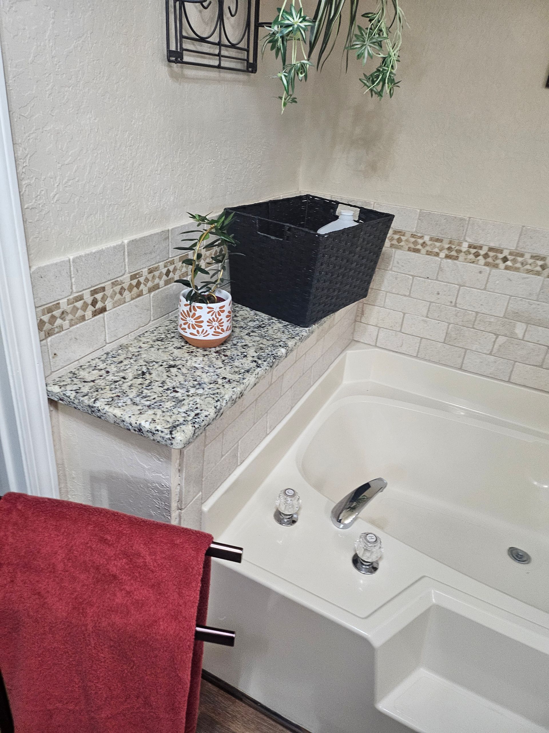 Bathroom with a bathtub, granite countertop, and red towel. Includes a black bin and a potted plant.