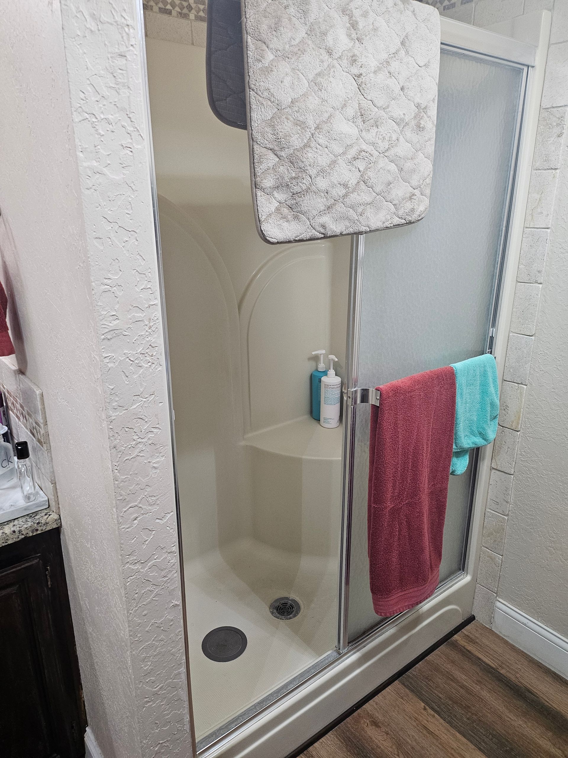 Shower with sliding glass doors, towels hanging, soap bottles, and a seat.