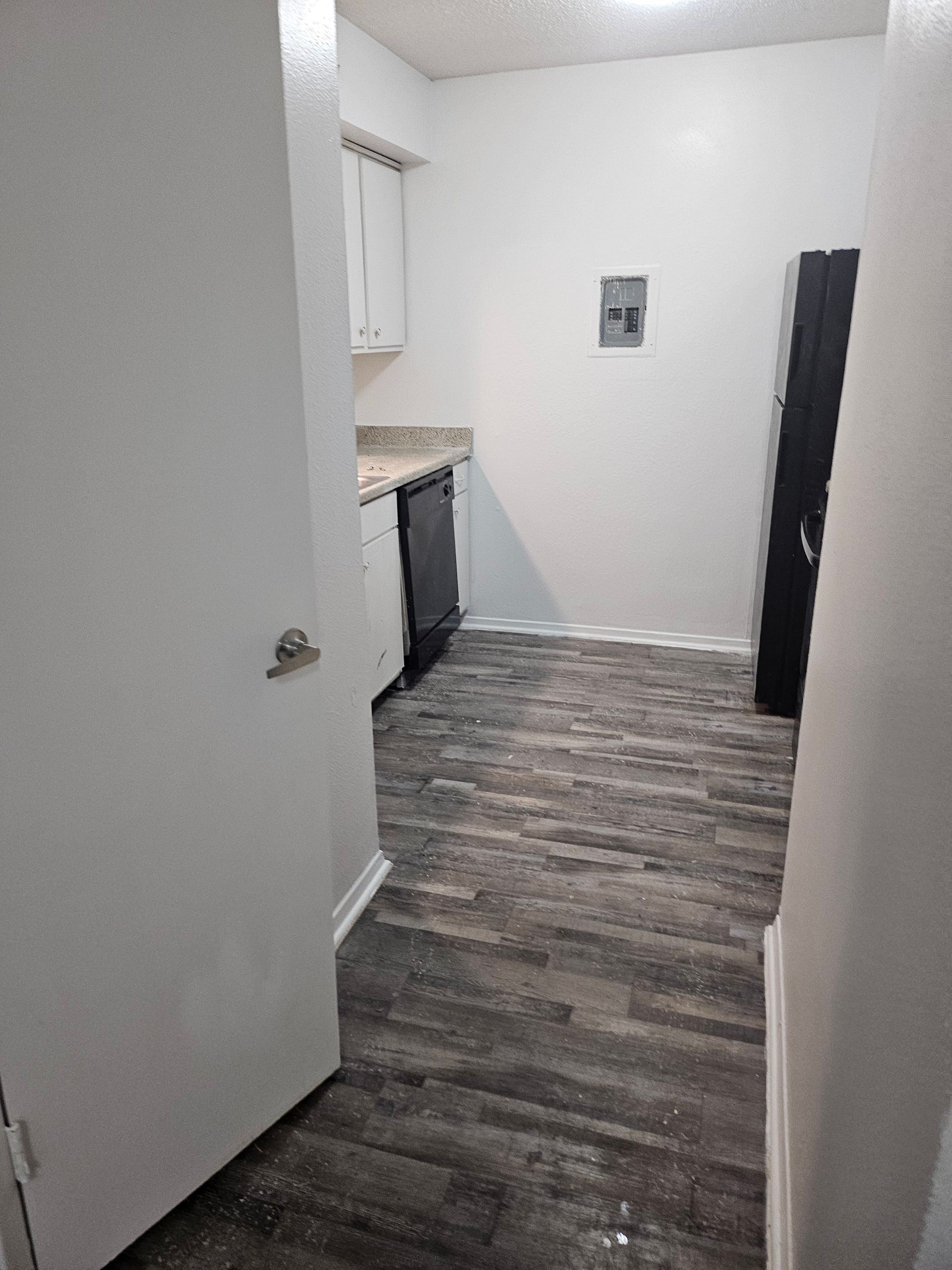 Narrow kitchen with dark wood-look flooring, white cabinets, and a black appliance. A closet is on the right.