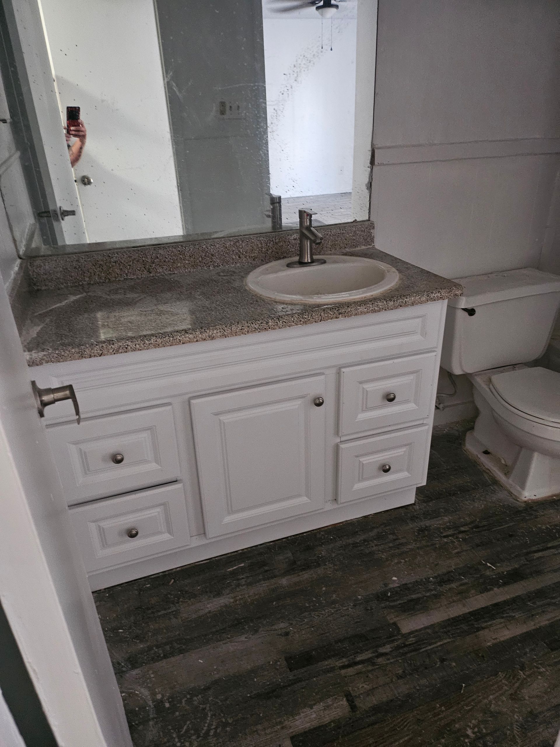 White vanity with granite countertop and sink in a bathroom. Dark wood-look floor.
