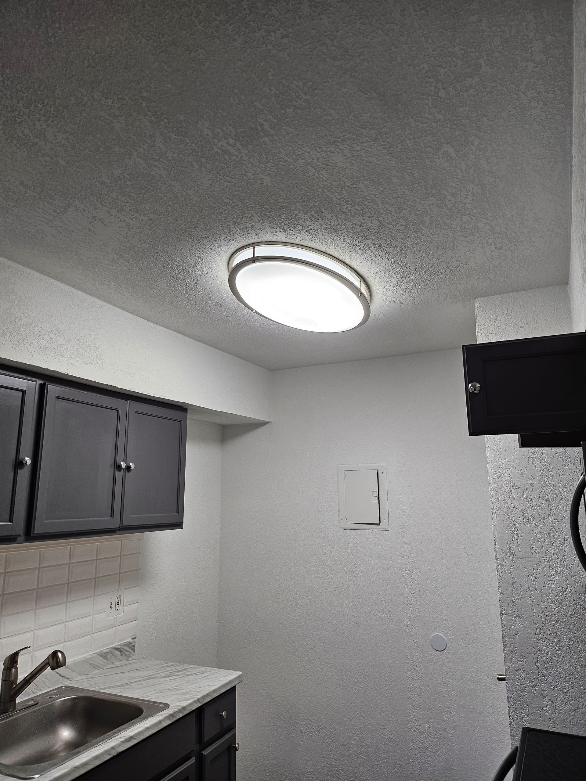 Kitchen with cabinets, sink, and ceiling light. Gray countertops, white walls, and a textured ceiling.