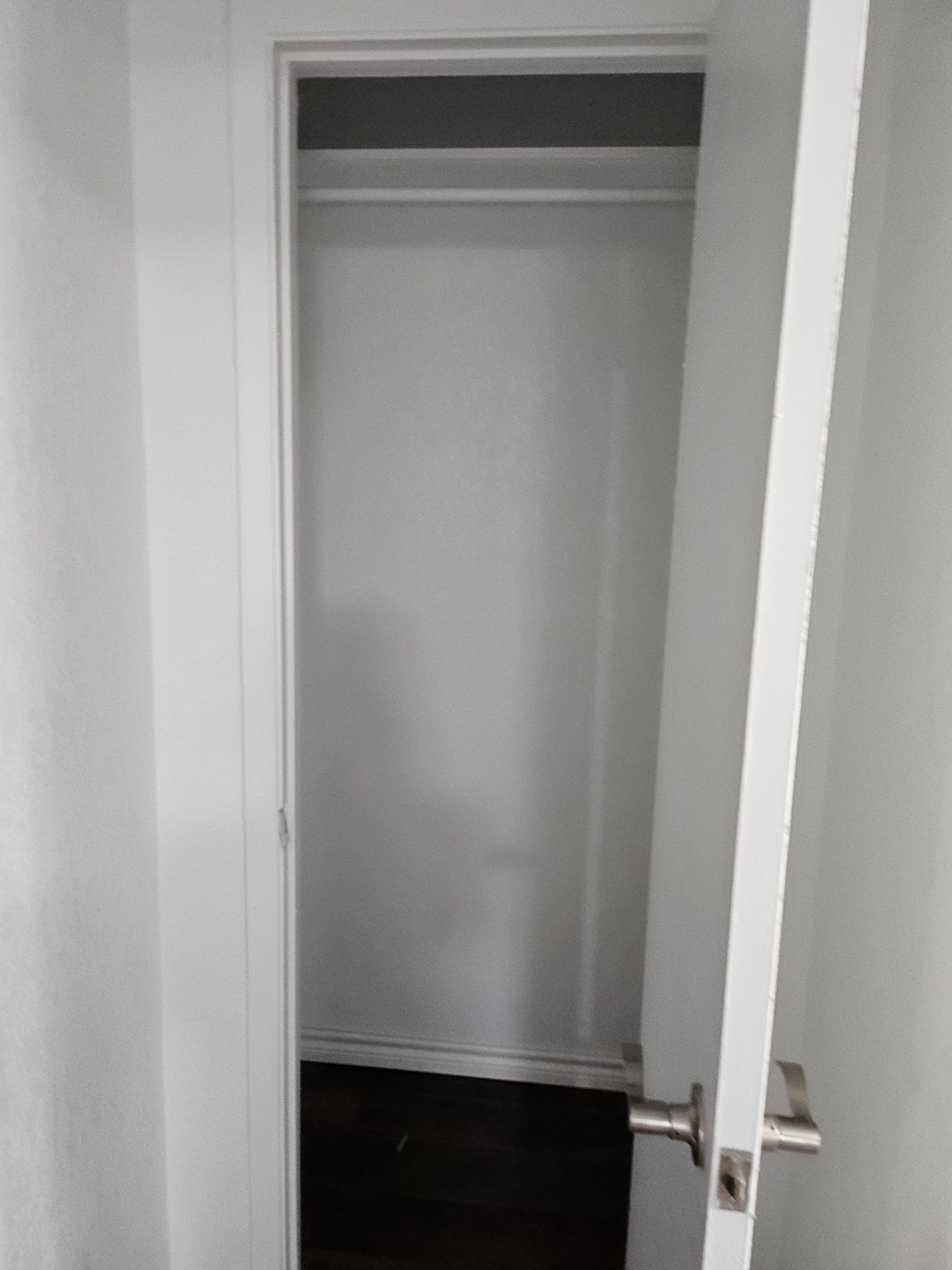 Open white closet door, empty closet interior with dark flooring, white walls, and a hanging rod.