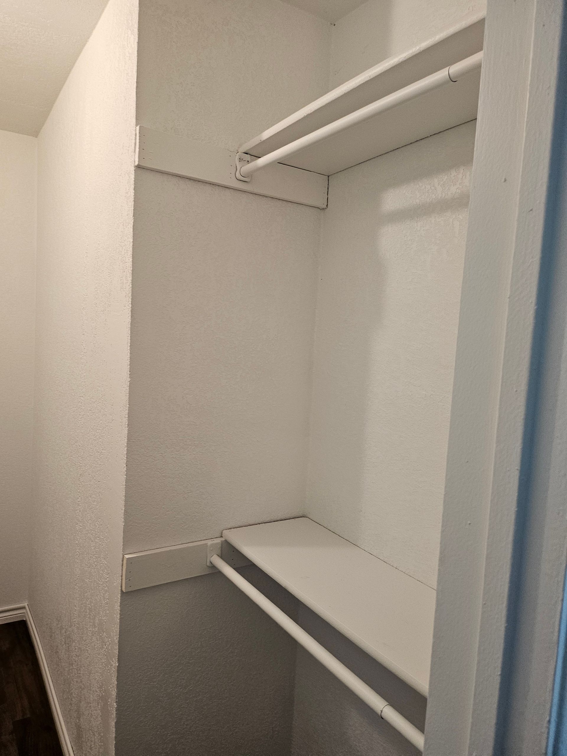 Empty white closet with top shelf and hanging rod, bottom shelf visible.