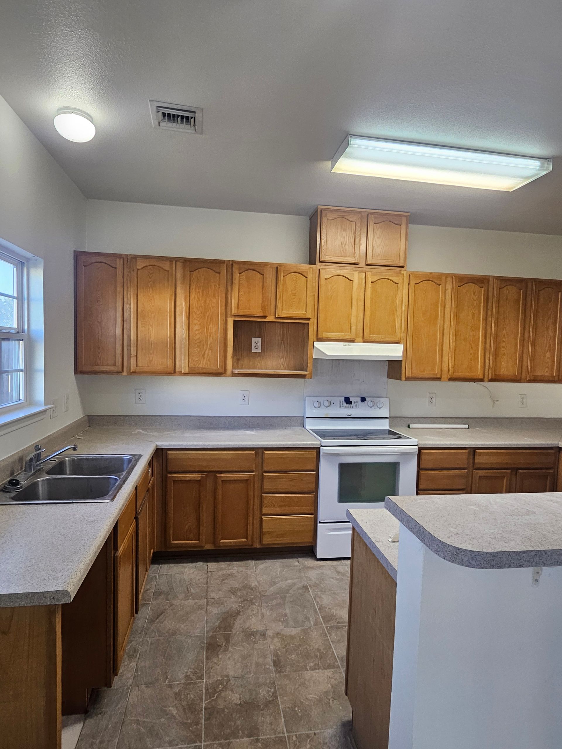 A kitchen with light brown cabinets, white appliances, and a gray countertop.