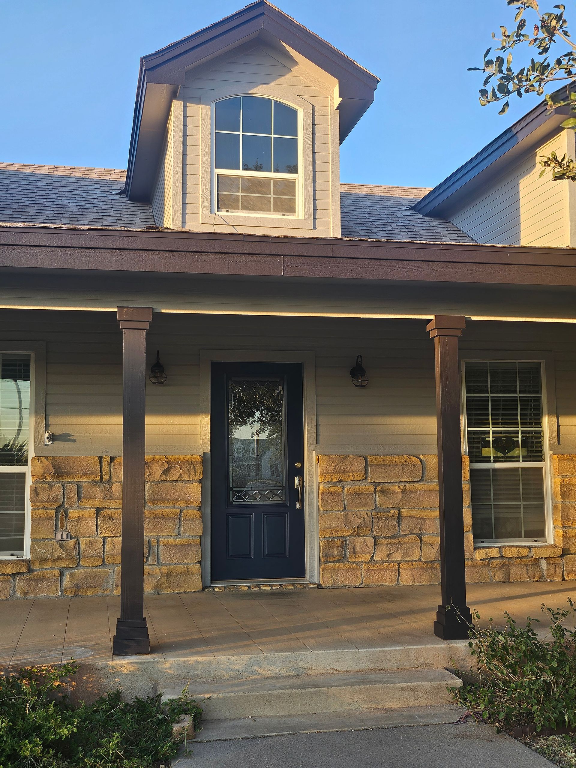 Front view of a house with stone accents, a dark blue door, and a dormer window.