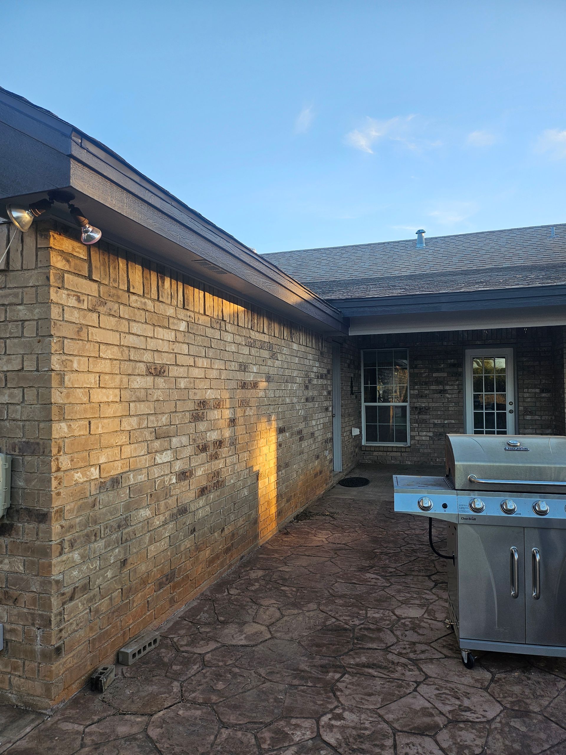Brick building exterior with a patio, grill, and clear sky.