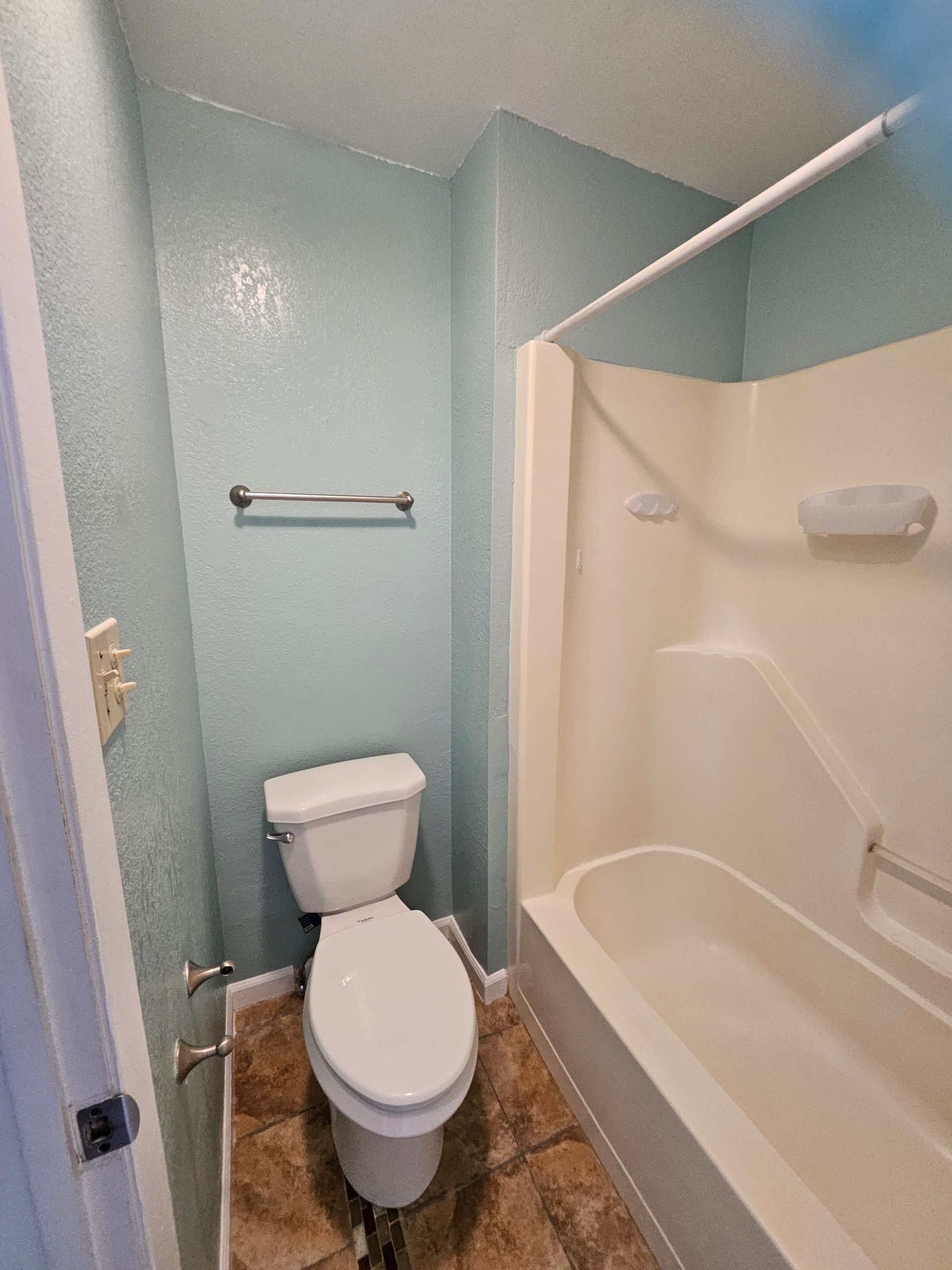 Small bathroom with blue walls, white toilet, and beige tub.