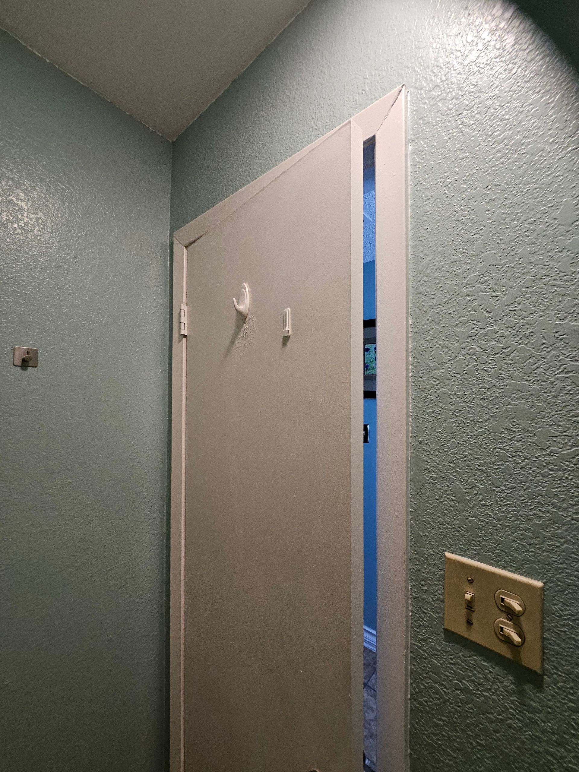 White door slightly ajar in a room with textured, light blue walls. Electrical outlet visible.