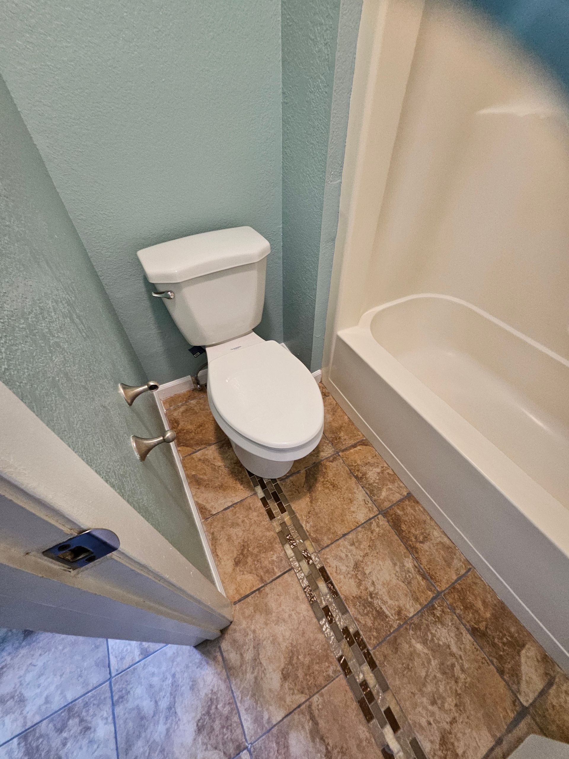 Toilet in a bathroom with beige tile floor and blue wall; a white bathtub is to the right.
