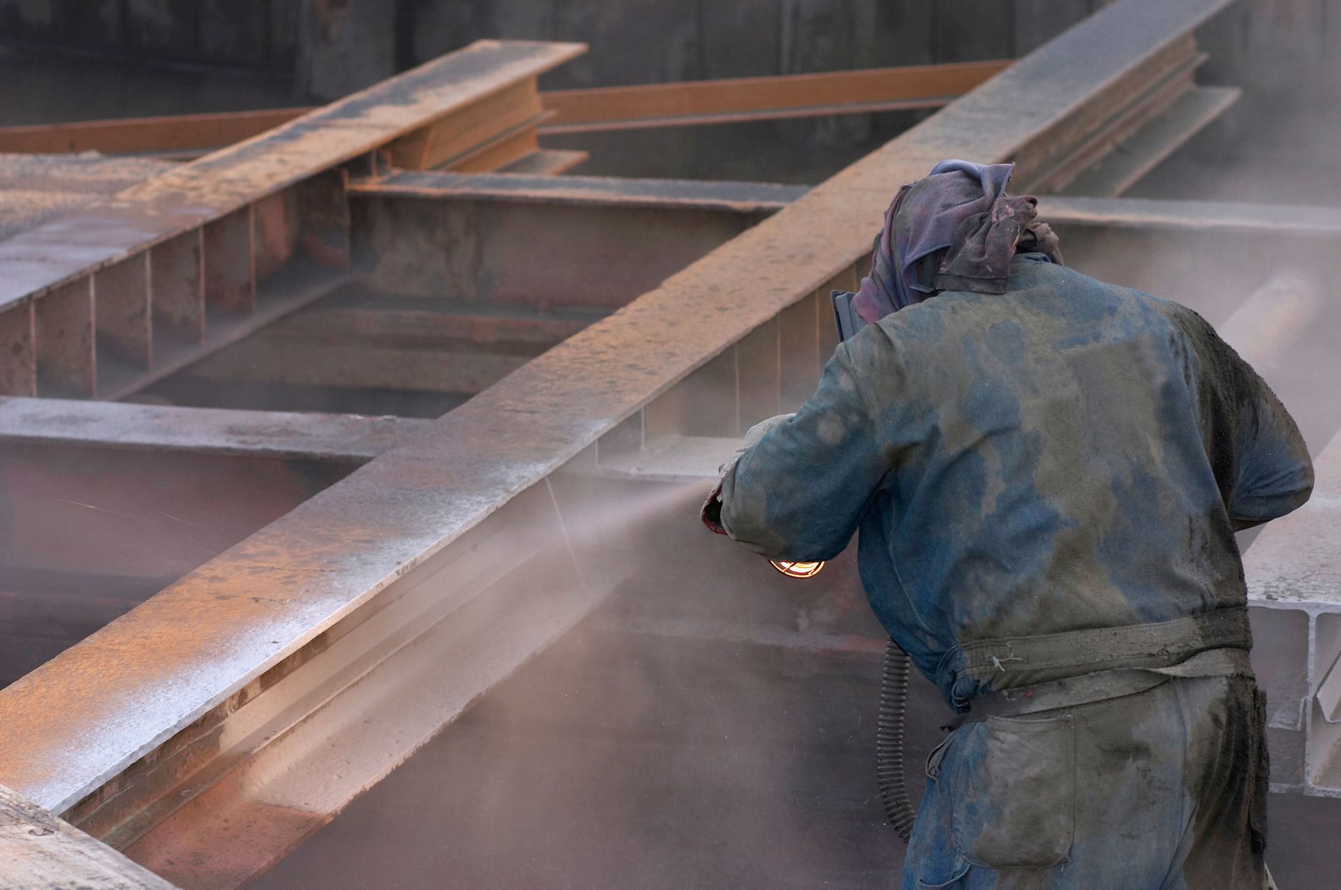 A man wearing a mask is sandblasting a metal structure.