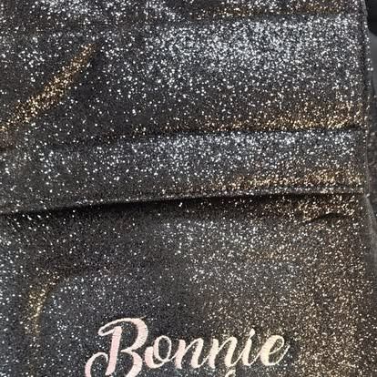 A close up of a black and gold glitter backpack with the name bonnie embroidered on it.

