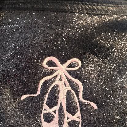 A pair of pink ballet shoes with a bow on a black background.