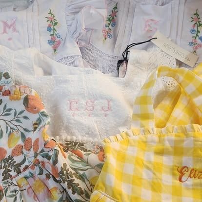 A pile of clothes including a yellow and white checkered dress with the letters csj embroidered on it