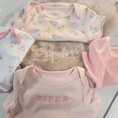 A pile of pink and white baby clothes with the name piper embroidered on them.