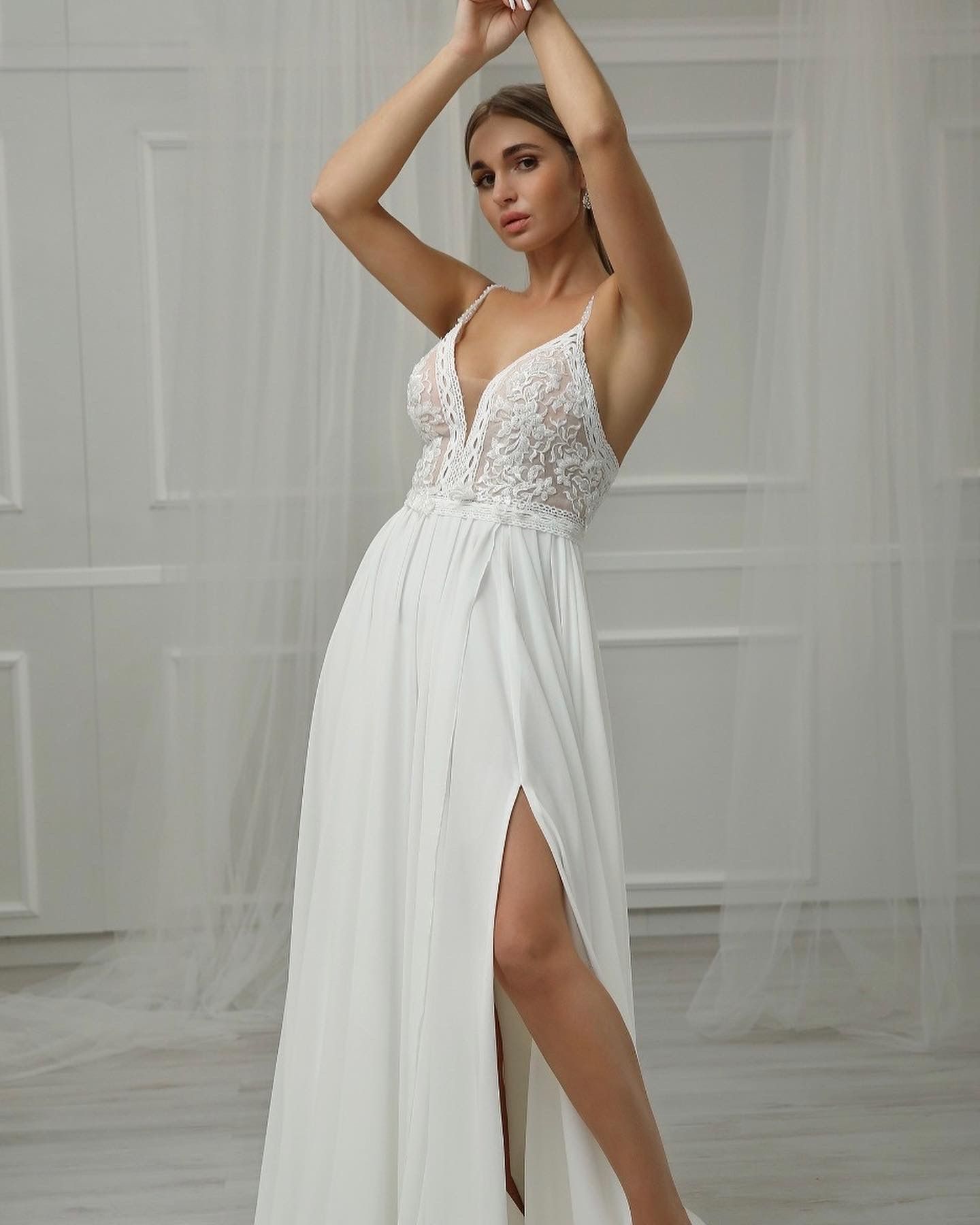 Eine Frau in einem weißen Kleid mit hohem Schlitz steht vor einer weißen Wand.