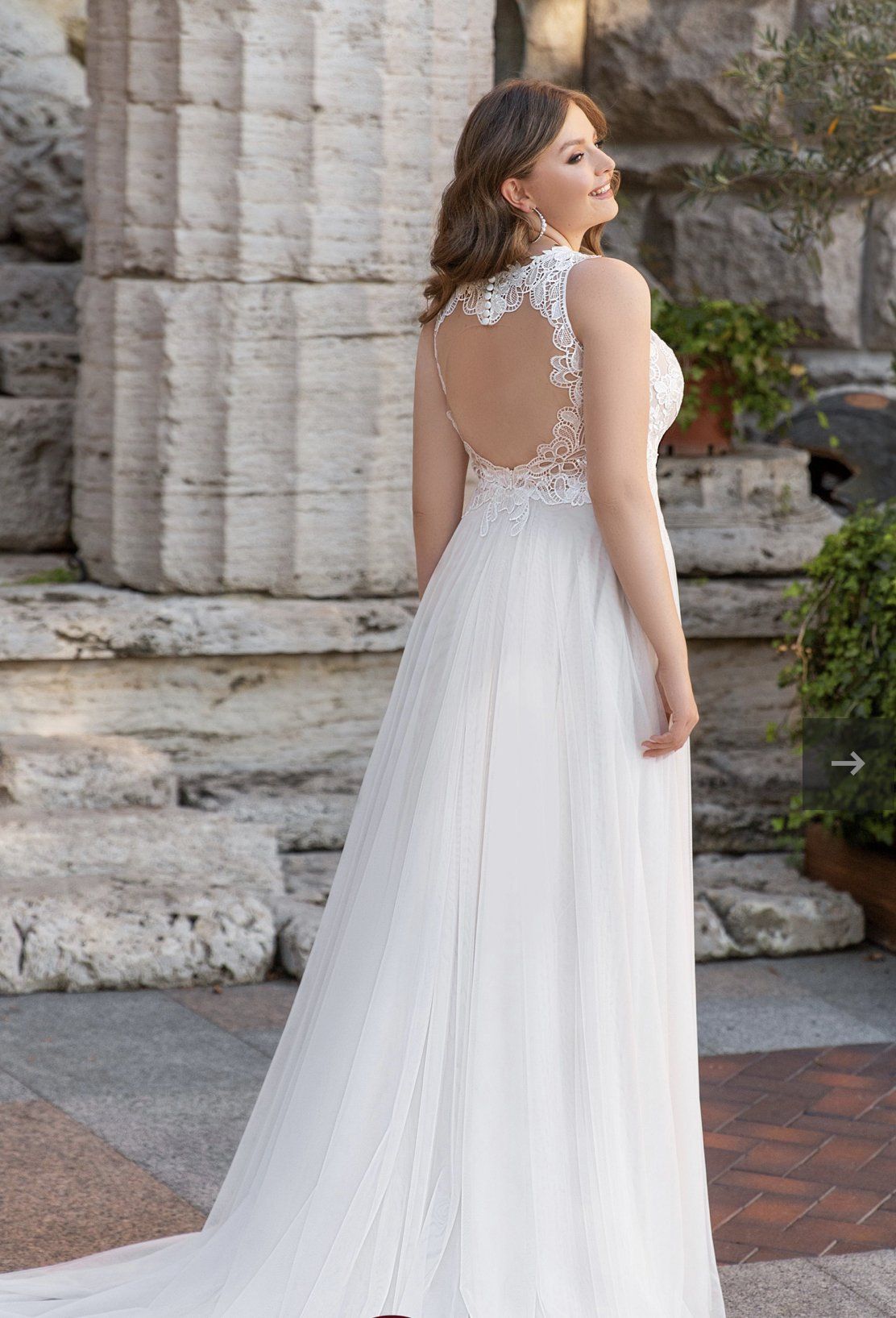 Eine Frau in einem weißen Hochzeitskleid steht vor einer Steinmauer.