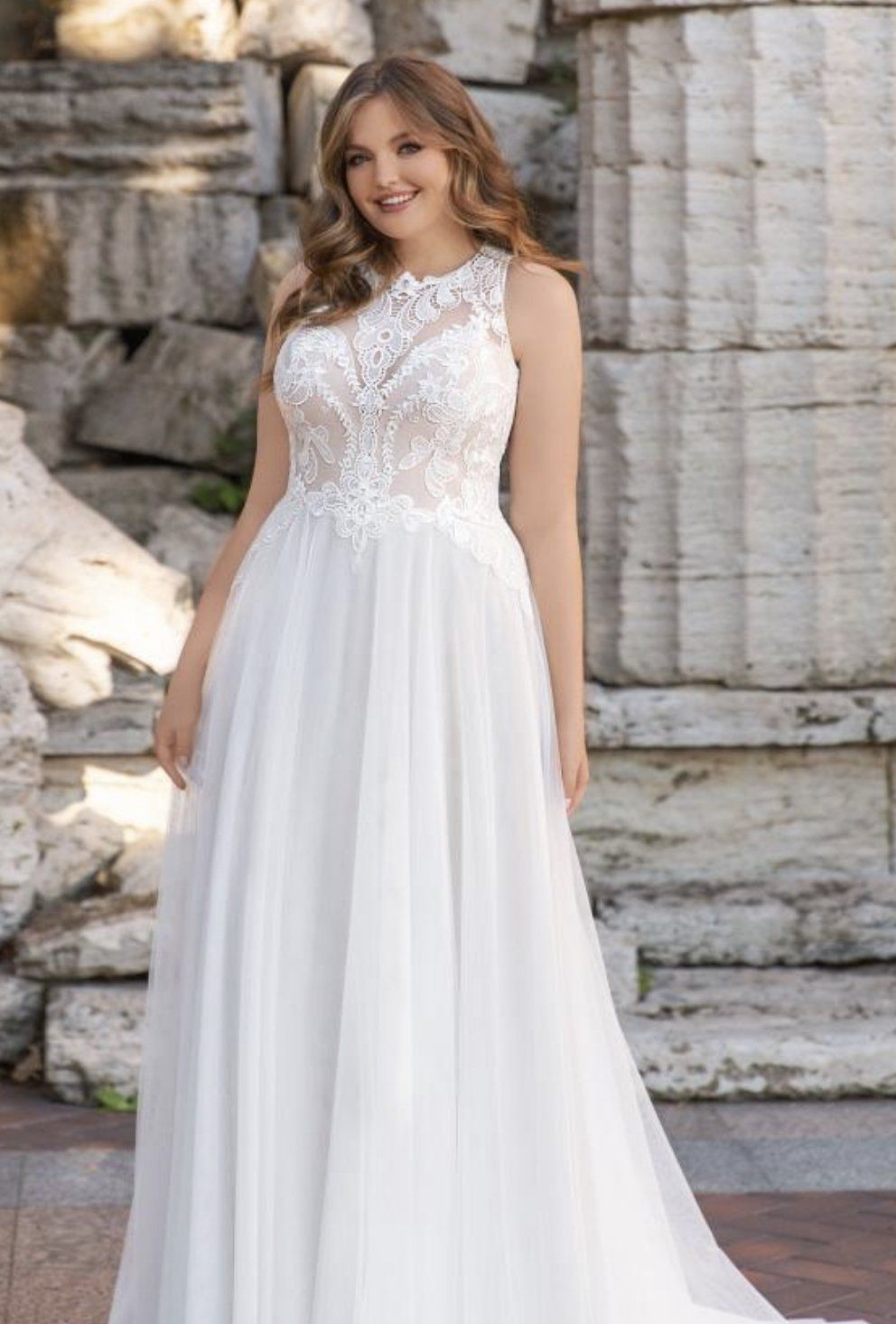 Eine Frau in einem weißen Hochzeitskleid steht vor einer Steinmauer.