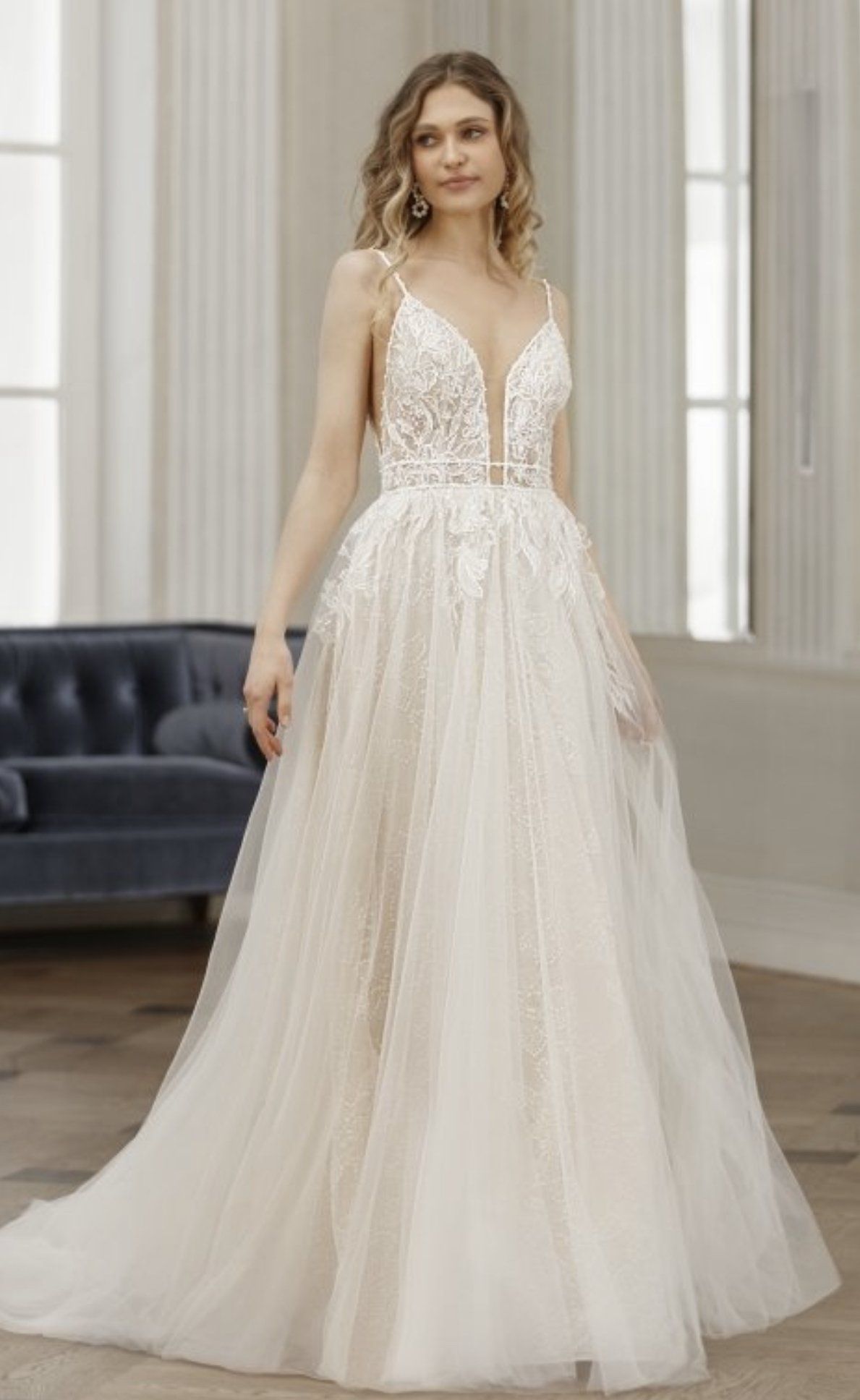 Eine Frau in einem Brautkleid steht vor einem blauen Sofa.