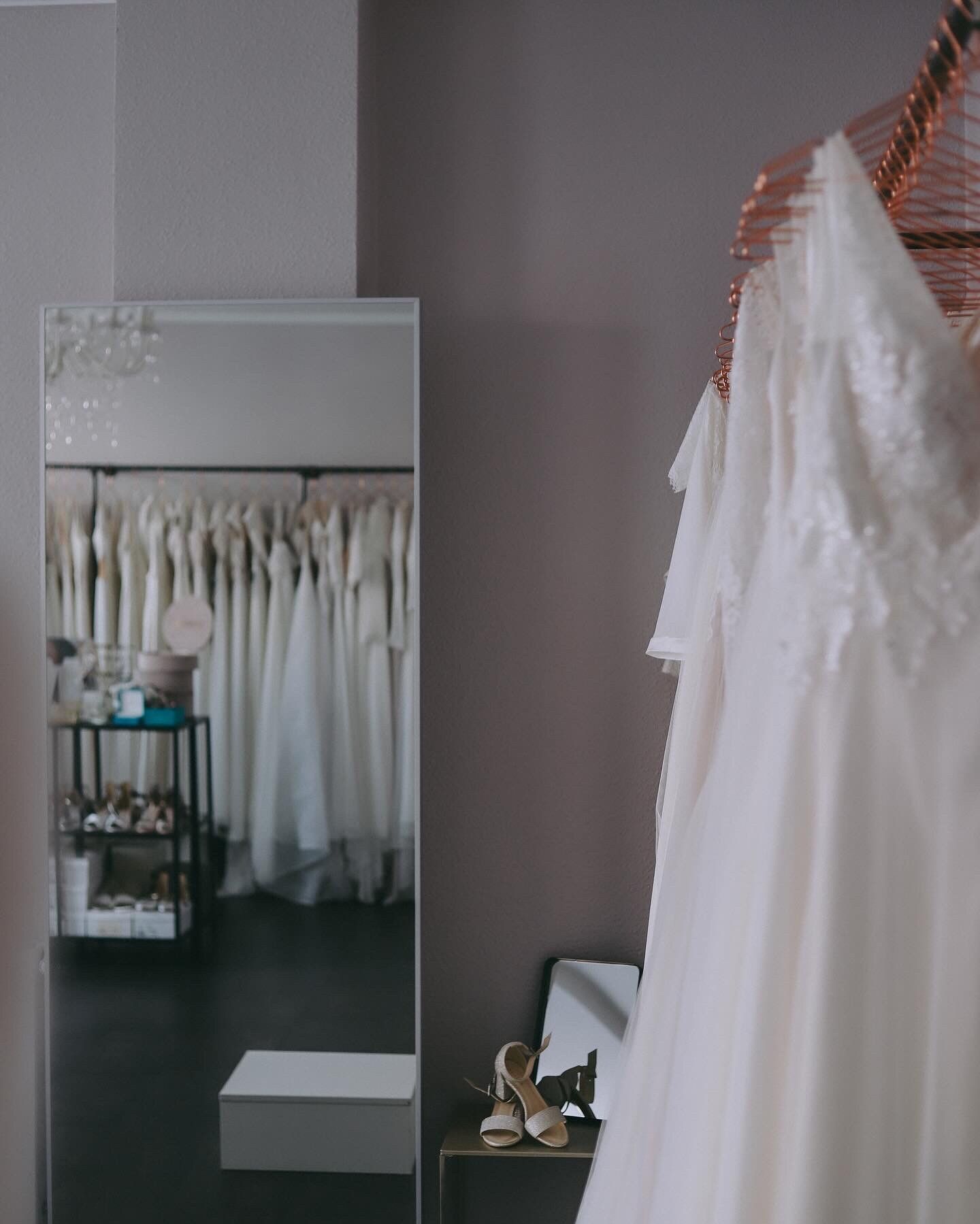 Ein weißes Kleid hängt vor einem Spiegel in einem Zimmer.