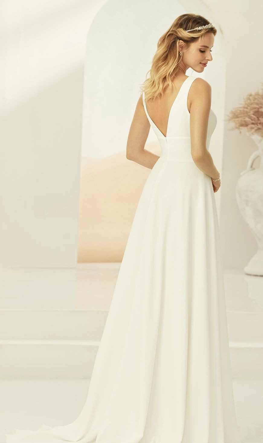 Eine Frau in einem weißen Brautkleid steht vor einer Vase.