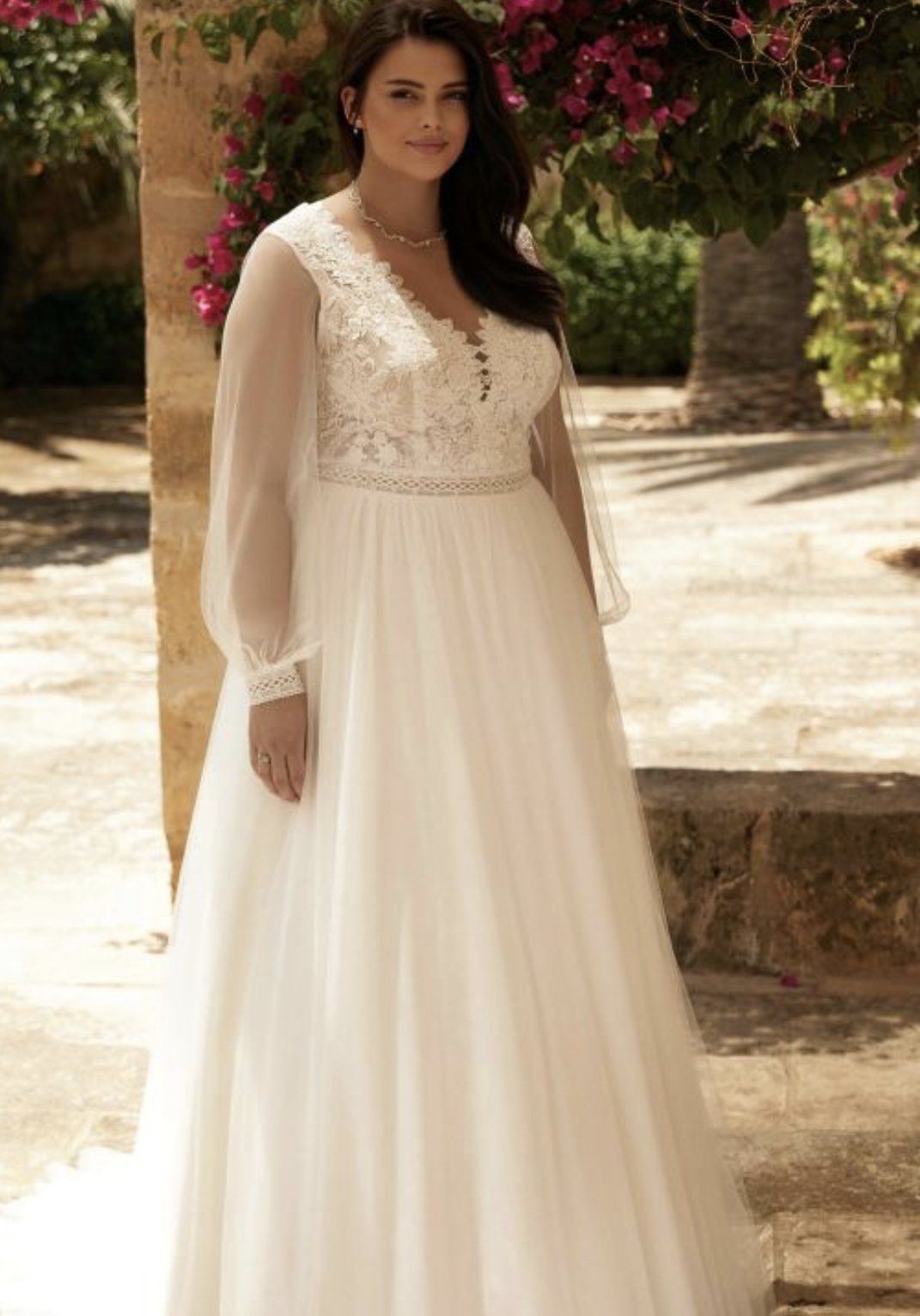 Eine Frau mit Übergröße trägt ein weißes Hochzeitskleid mit langen Ärmeln.