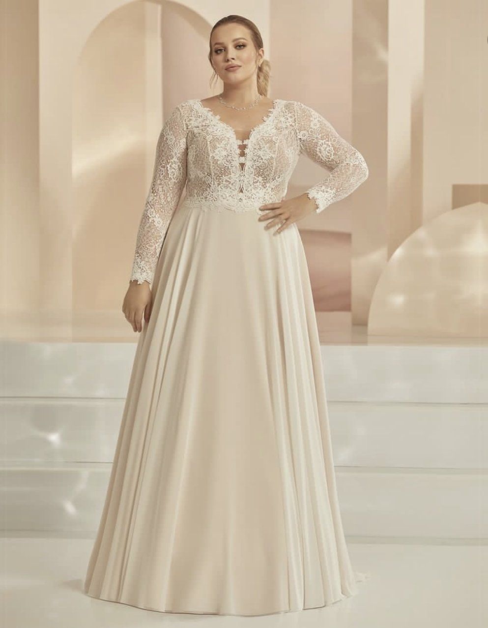 Eine Frau mit Übergröße trägt ein weißes Hochzeitskleid mit langen Ärmeln.