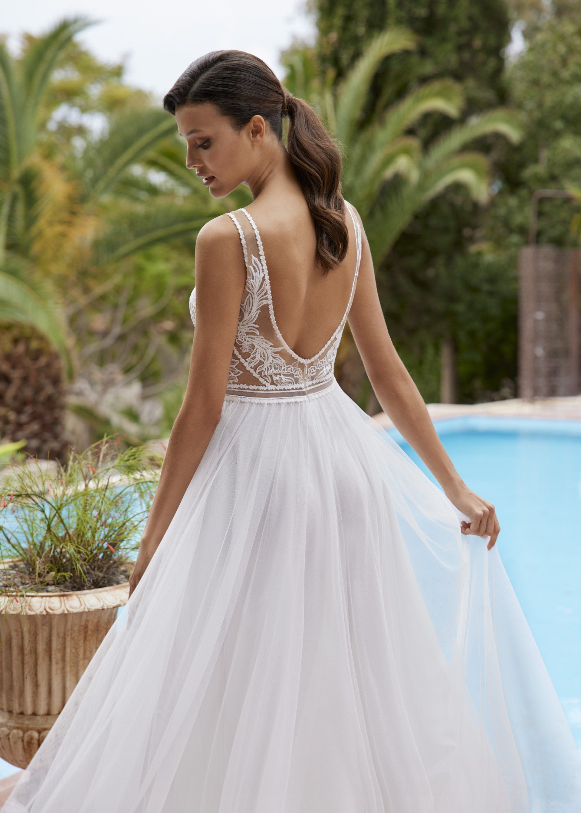 Eine Frau in einem weißen Hochzeitskleid steht neben einem Pool.