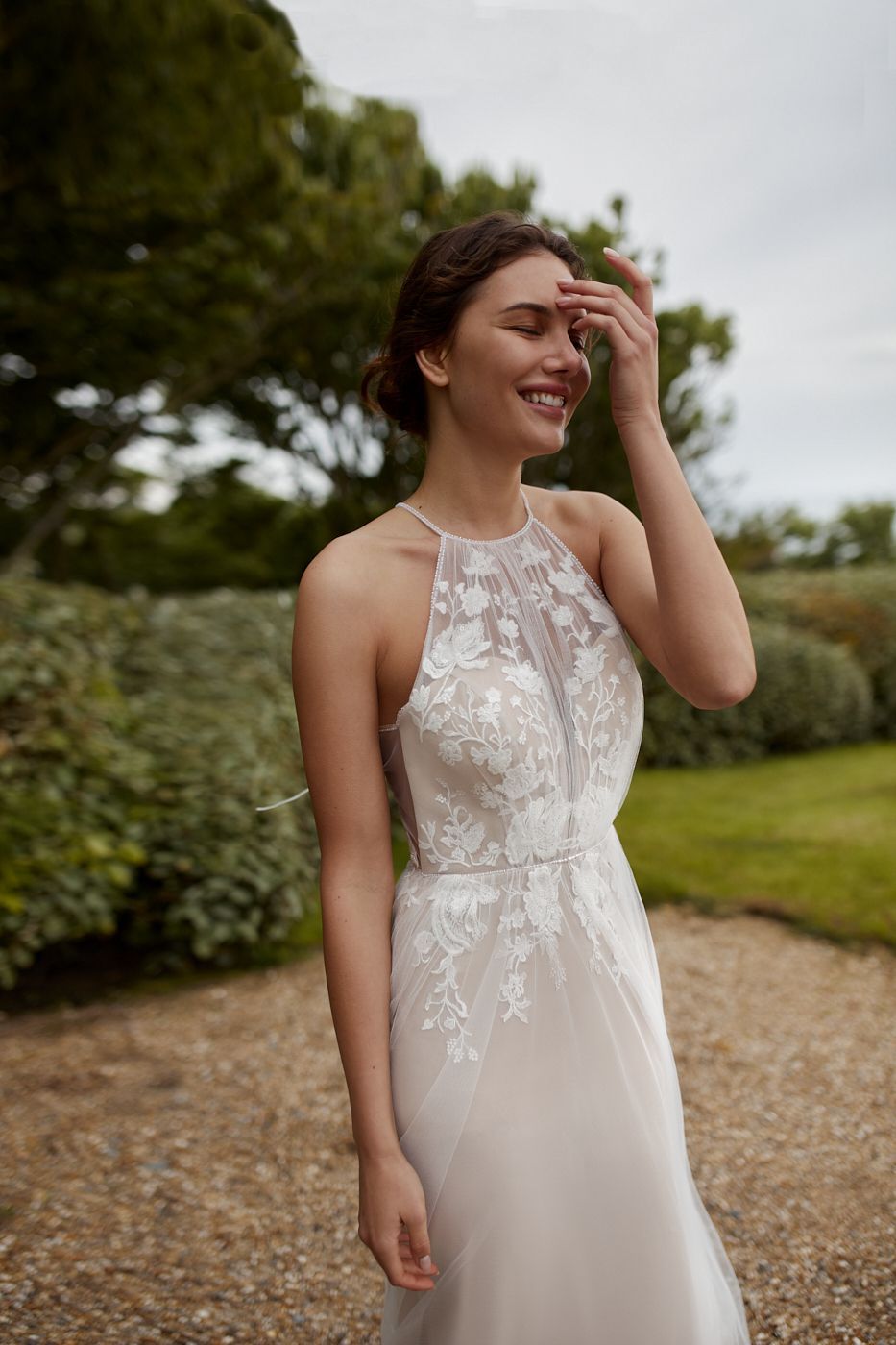 Eine Frau in einem weißen Brautkleid steht auf einer Kiesauffahrt.