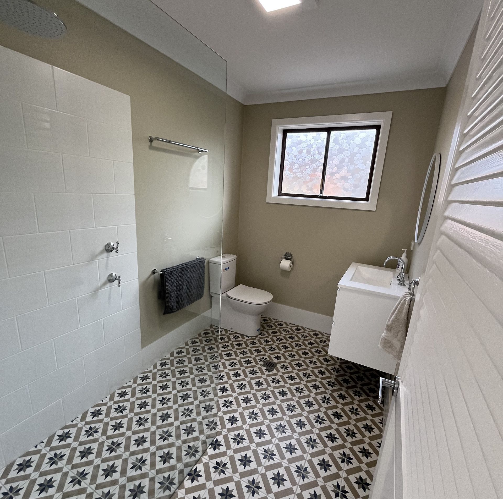 Bathroom with a patterned floor, white tiles in the shower, toilet, and sink | T Woods Plumbing