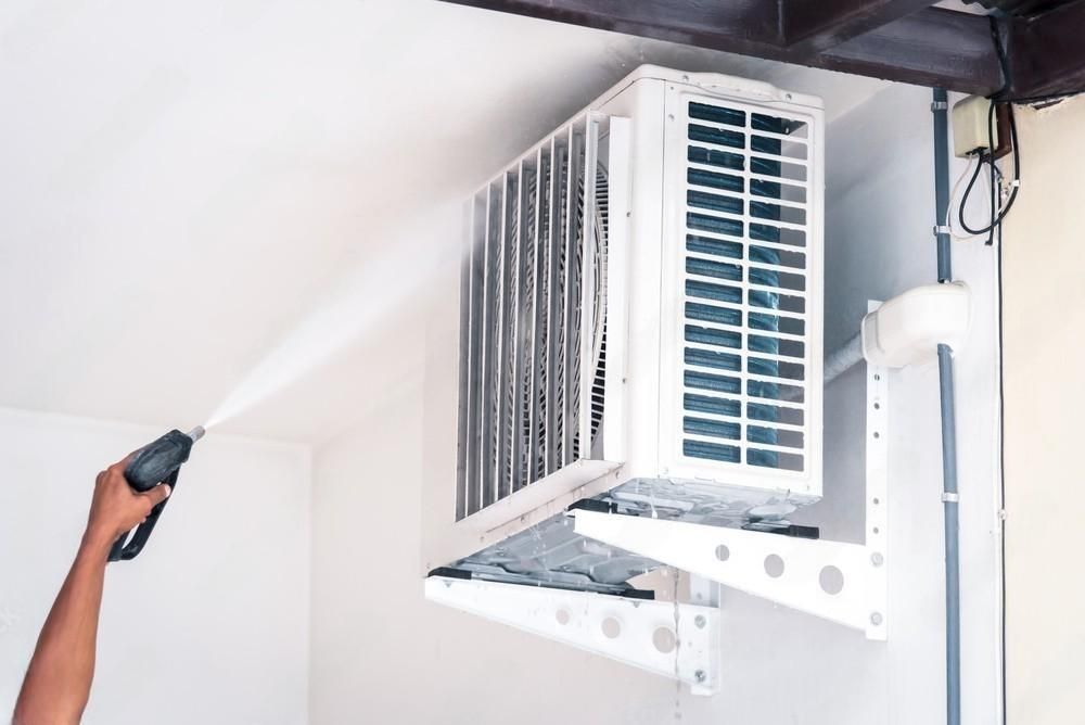 a person is cleaning an air conditioner with a high pressure washer .