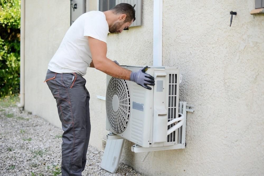 a man is installing an air conditioner on the side of a building .