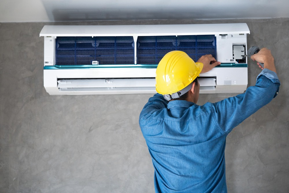 a man wearing a hard hat is working on an air conditioner .