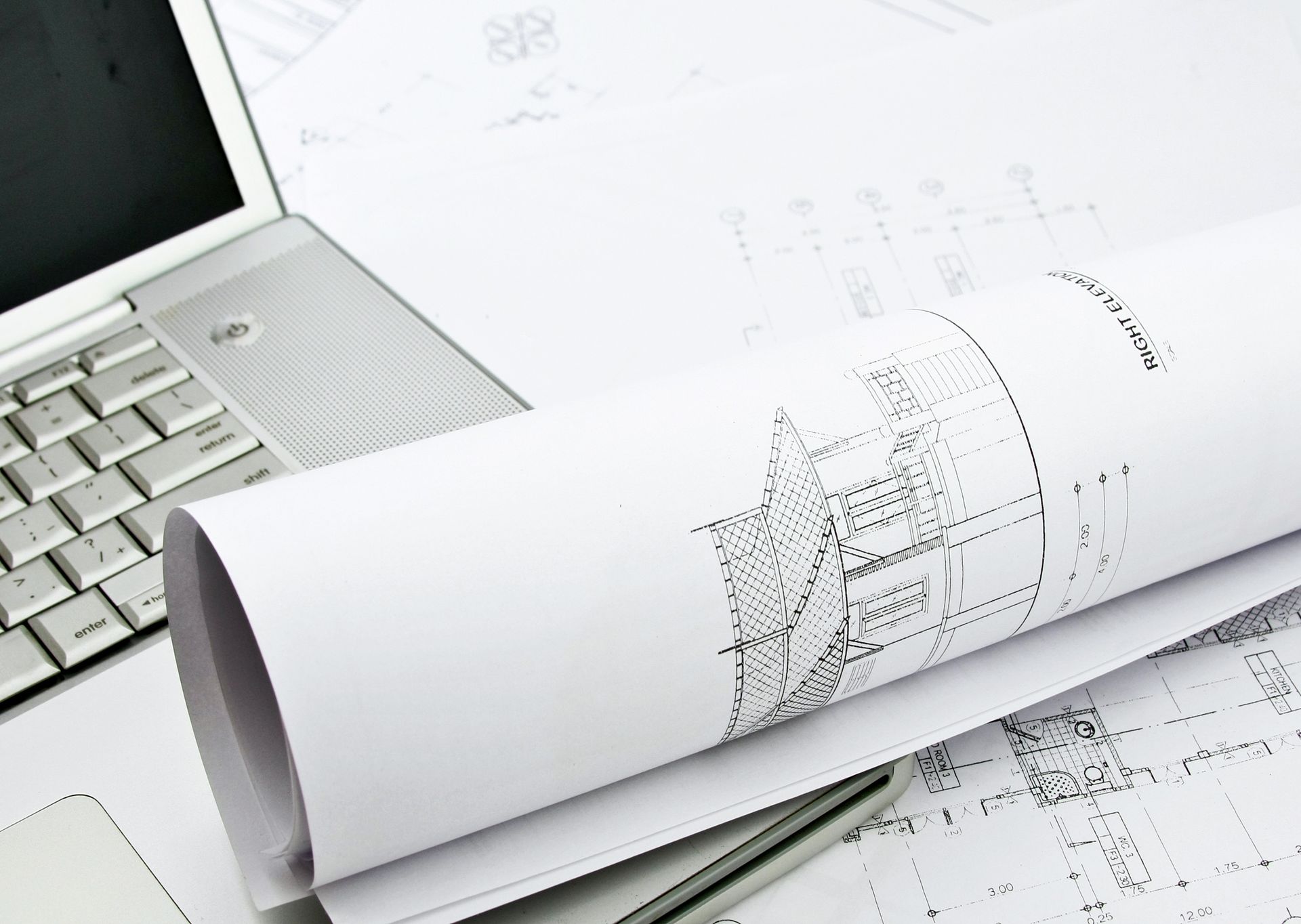 A drawing of a building is rolled up next to a laptop