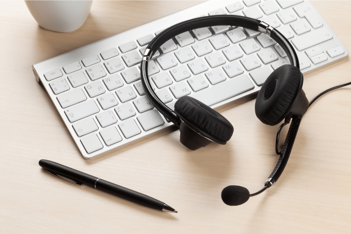A pair of headphones sitting on top of a keyboard next to a pen.