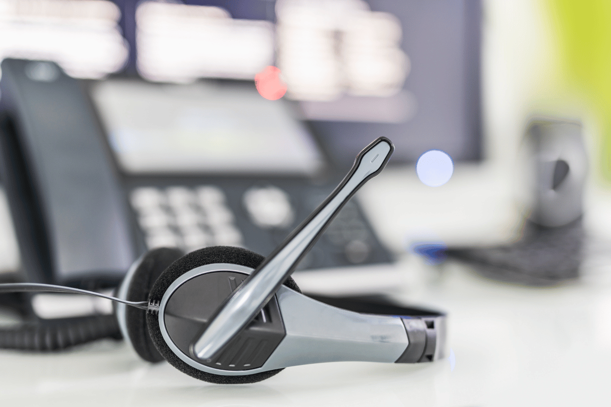 A headset is sitting on a desk next to a telephone.