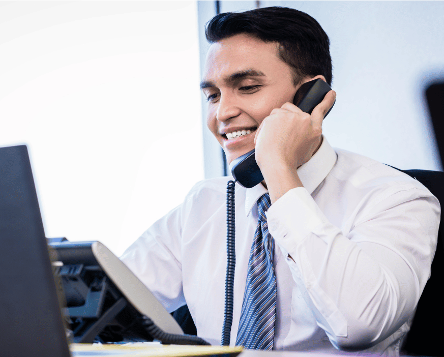 A man in a white shirt and tie is smiling while talking on a phone