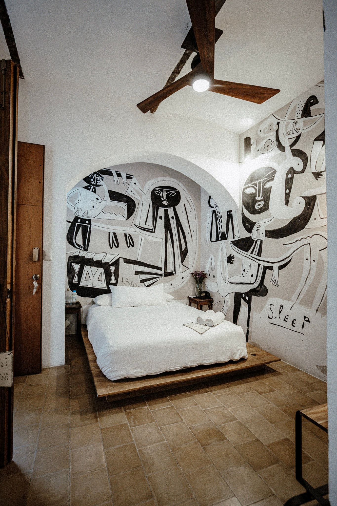 Small bedroom with white bed, wood floor, ceiling fan, and bold black-and-white wall murals.