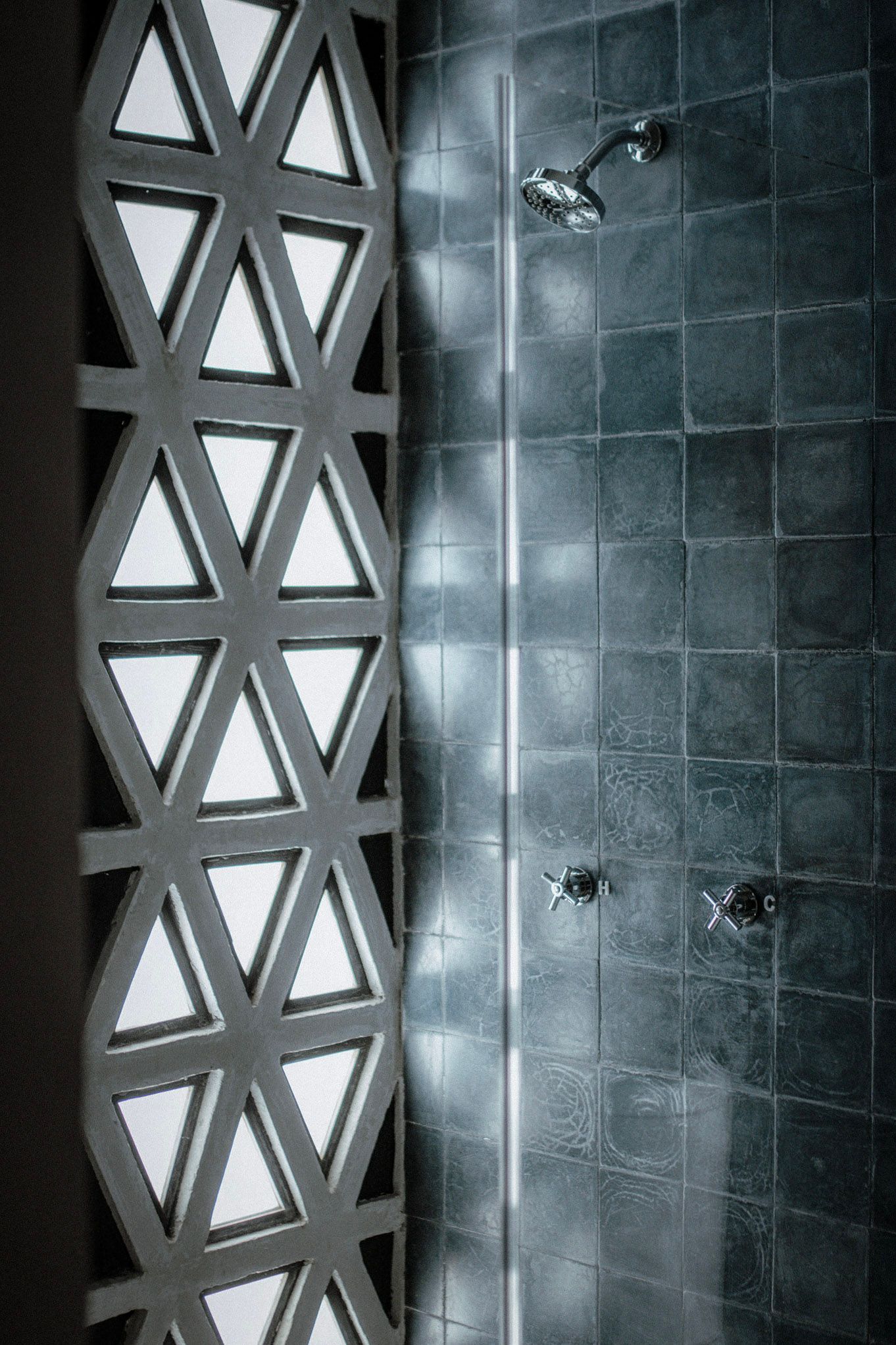 Gray tiled bathroom with shower fixtures beside a patterned geometric wall divider