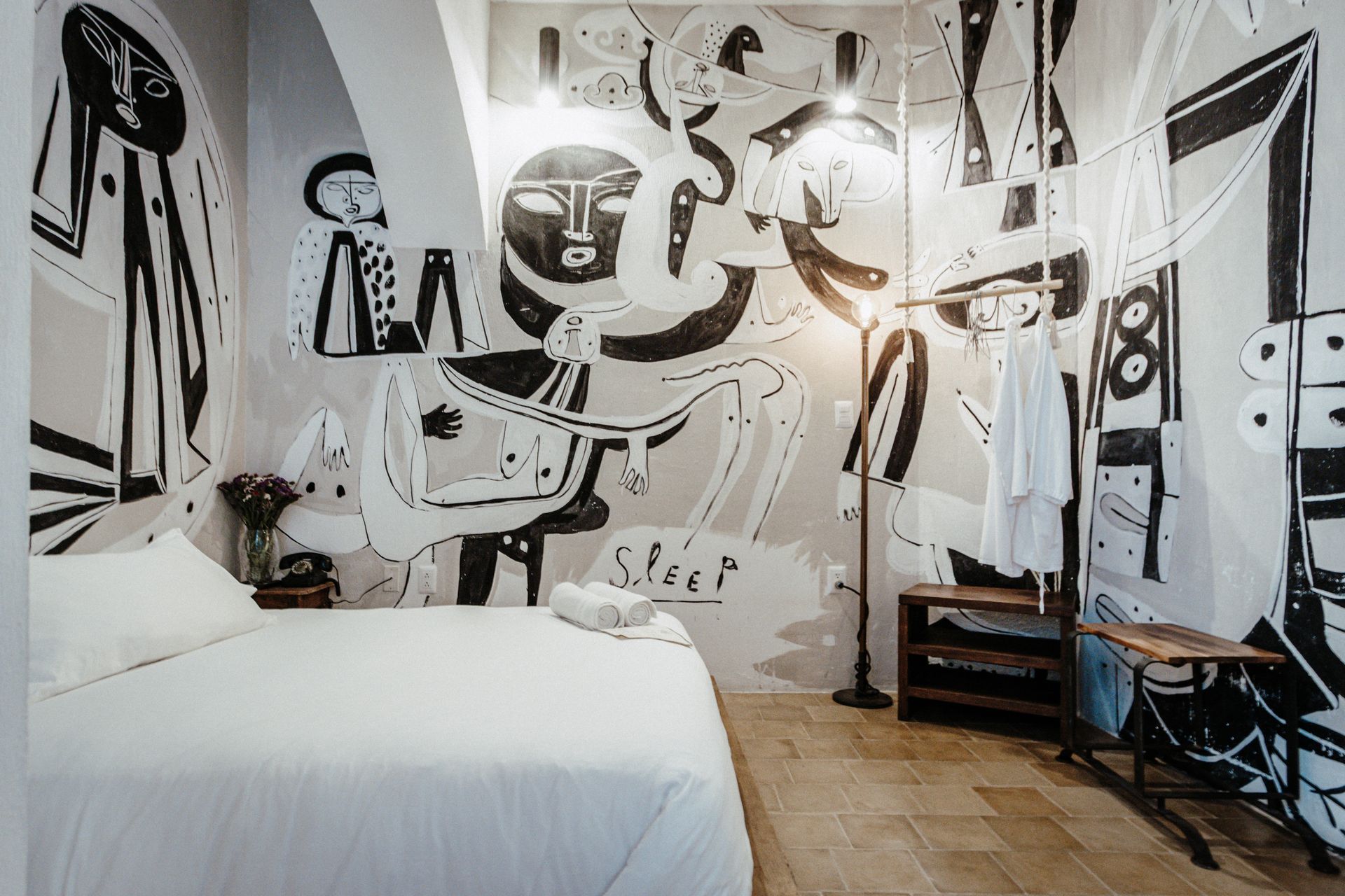 Modern bedroom with black-and-white abstract wall mural, white bed, and wooden floor
