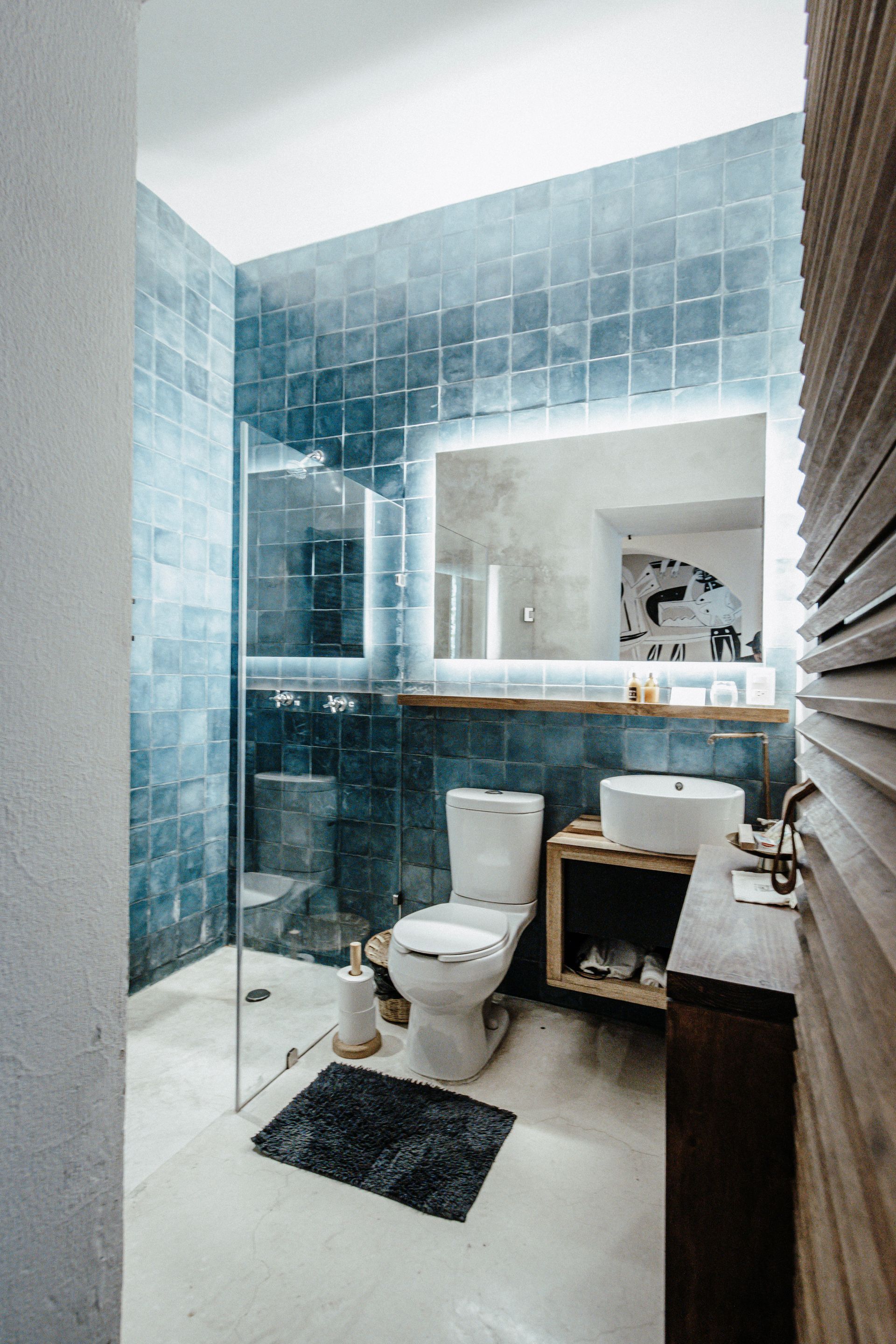 Modern bathroom with blue tile, glass shower, toilet, and sink vanity mirrored on the far wall