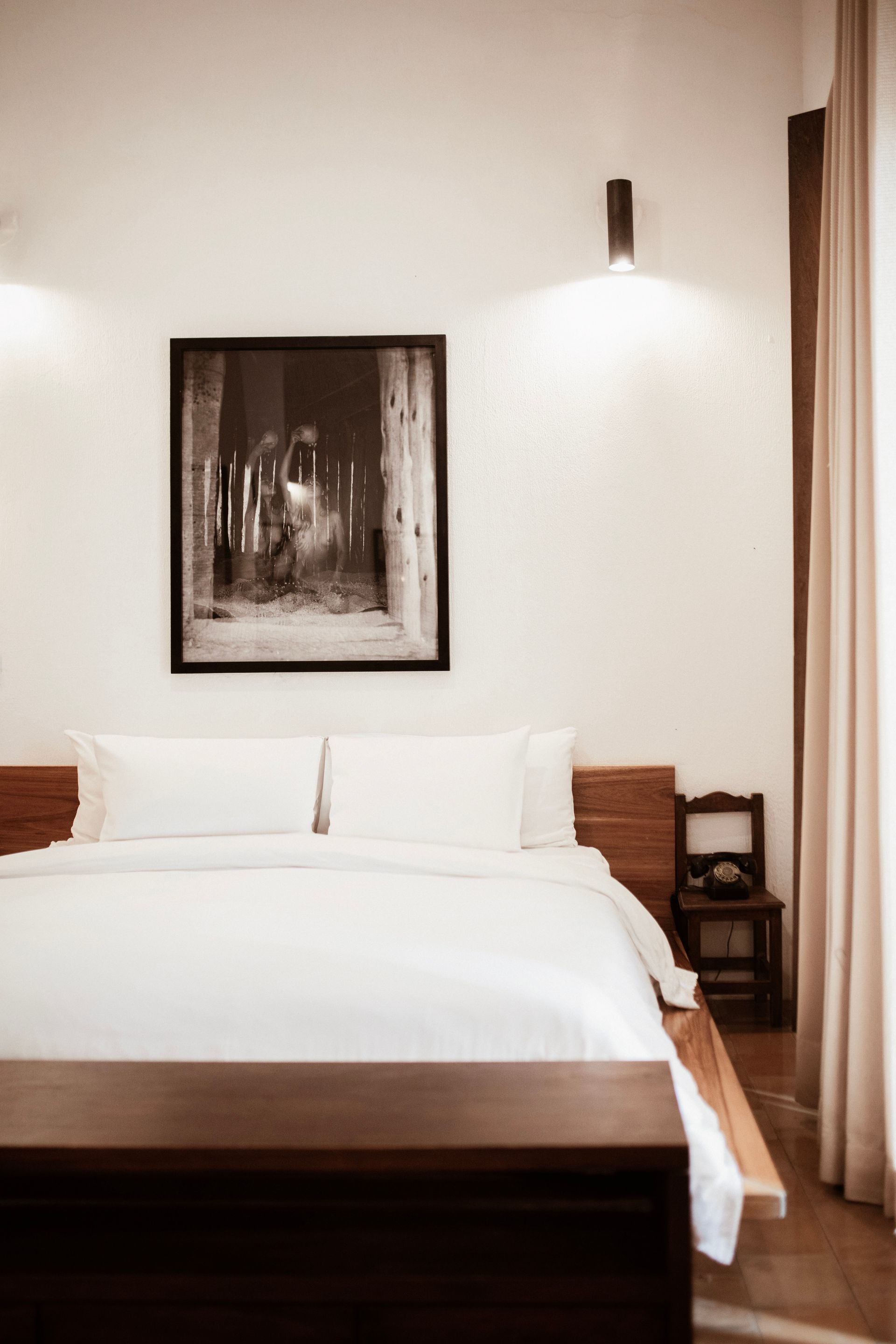 Minimal bedroom with white bed, framed artwork, and wall light beside wooden paneling